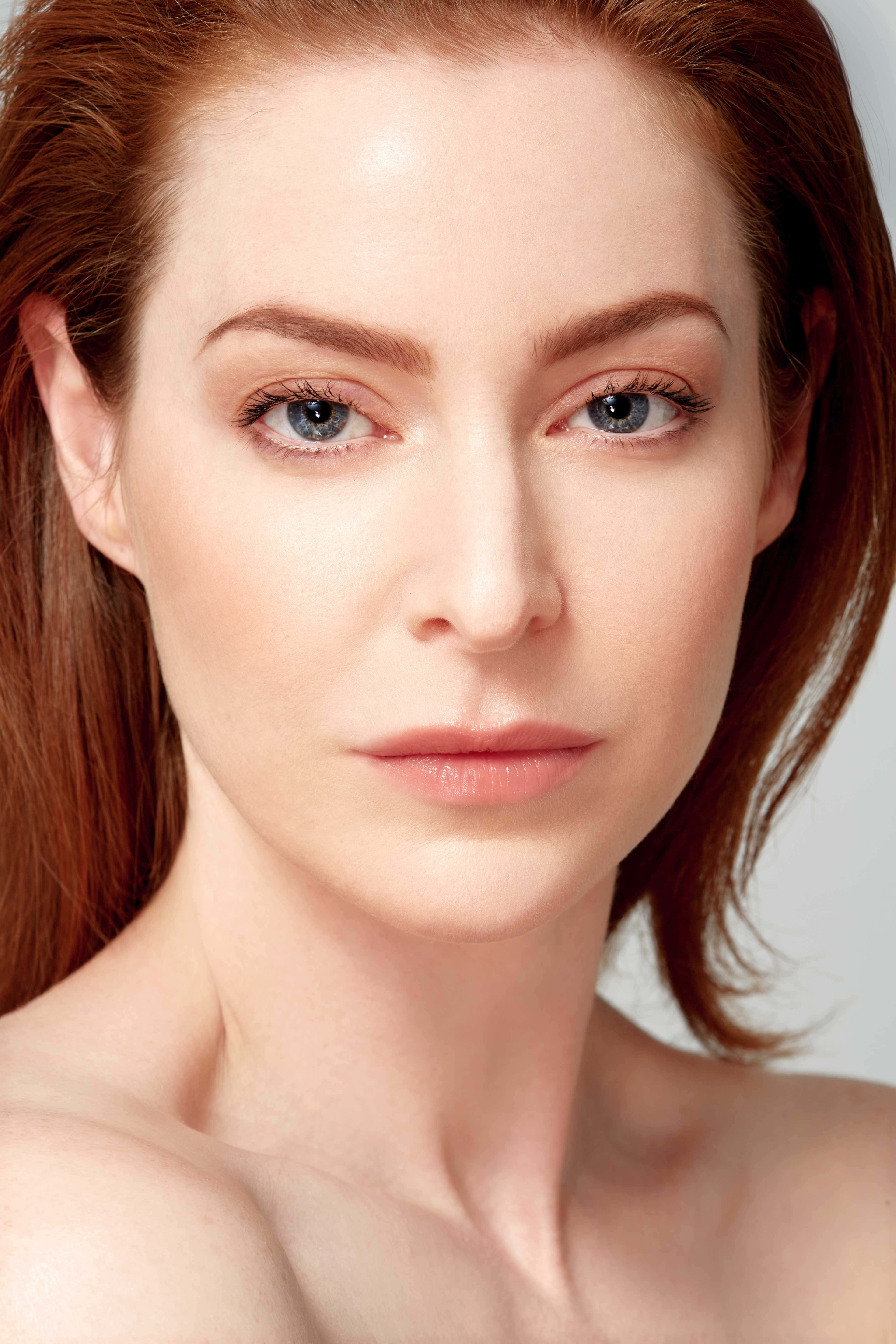 Esmé Bianco 桌布 壁紙 — 一位紅髮藍眼女性的特寫肖像，直視鏡頭，背景簡潔。