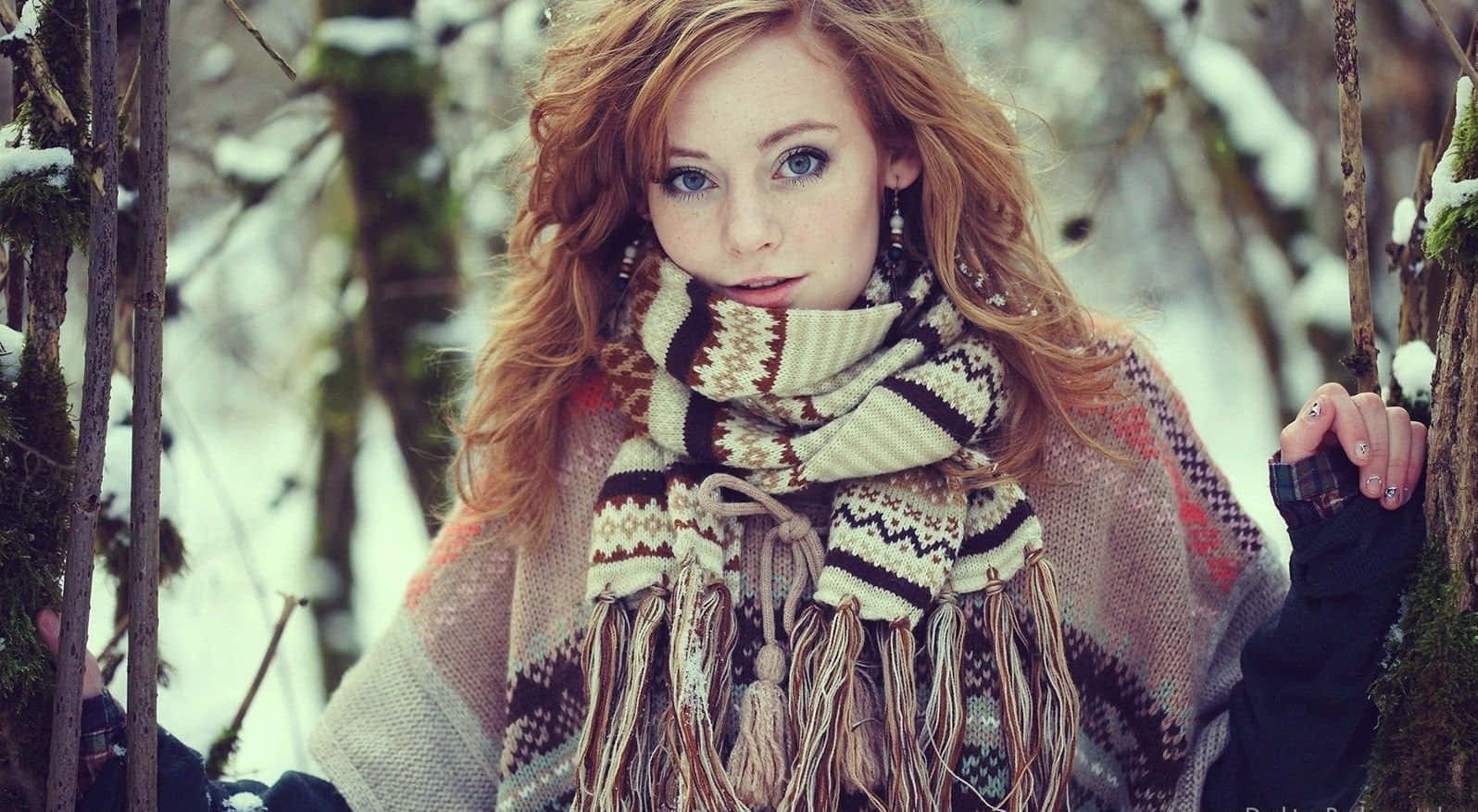 Winter Fashion 桌布 壁紙 — 一位紅髮藍眼的年輕女性在雪地森林中戴著圖案圍巾和針織毛衣。