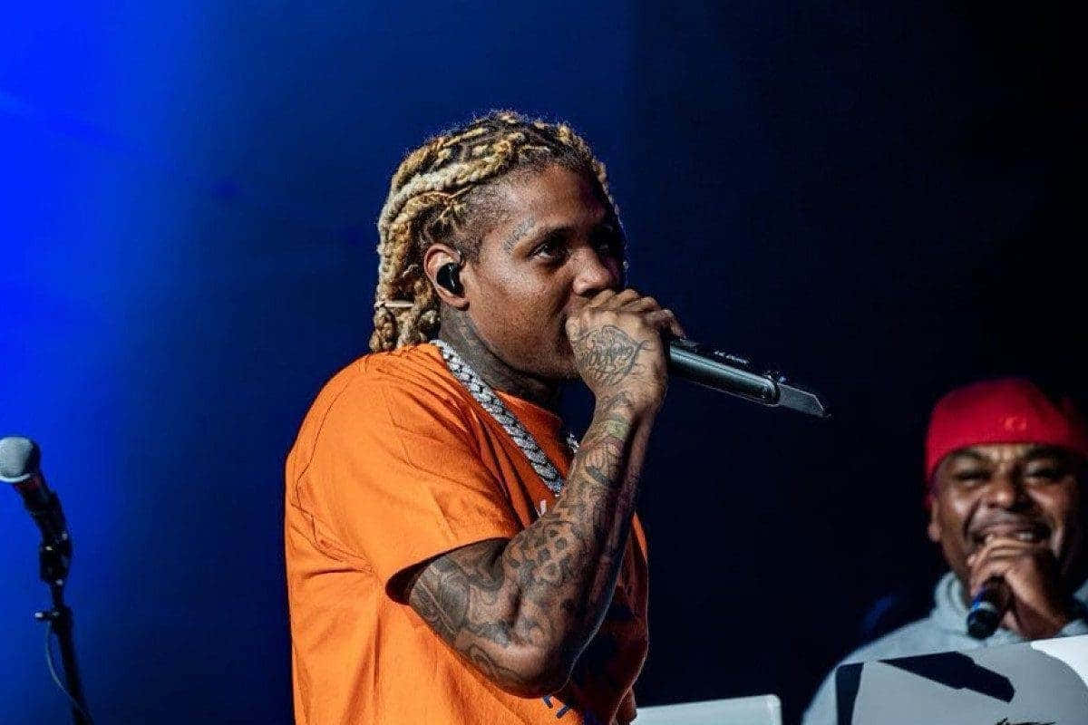  壁紙 — 一位紋身說唱歌手穿著橙色襯衫，在藍色舞台燈光下熱情地對著麥克風表演，旁邊有一位微笑的樂隊成員。