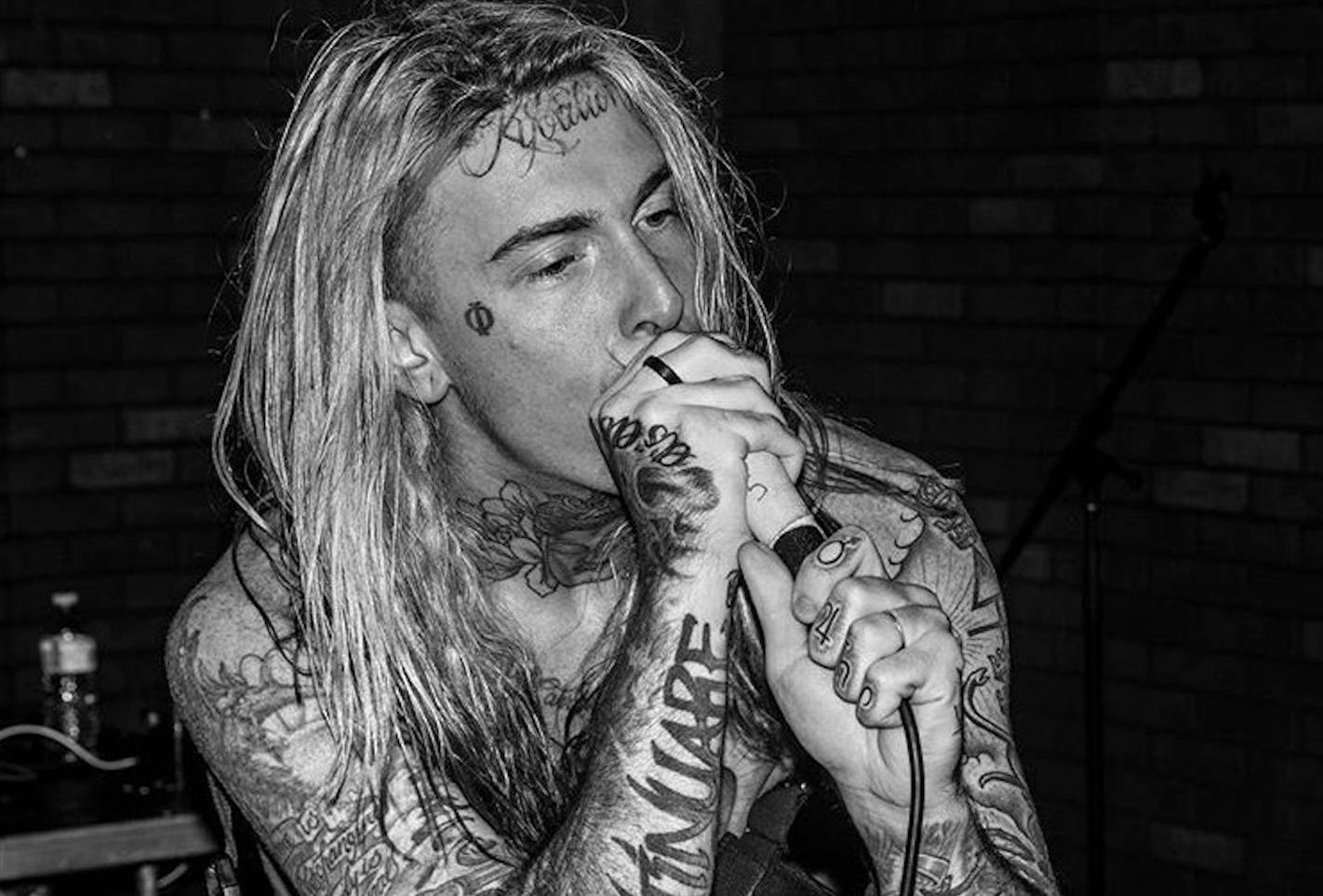Ghostemane 桌布 壁紙 — 一位紋身長髮音樂家對著麥克風熱情歌唱，背景是磚牆，黑白風格。