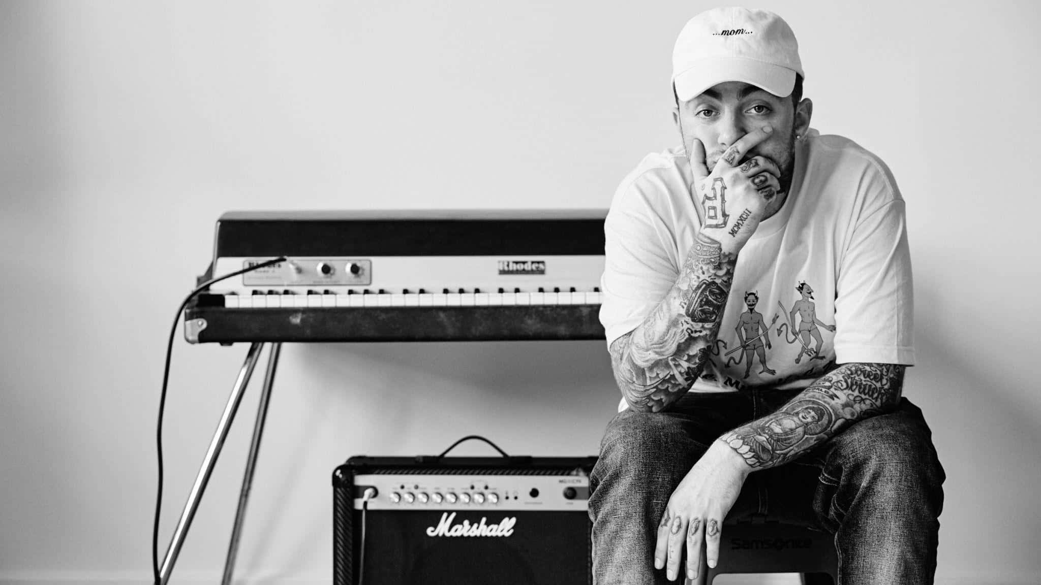 Mac Miller 桌布 壁紙 — 一位紋身音樂家戴著白色帽子，在極簡黑白工作室中若有所思地坐在鍵盤和 Marshall 擴音器旁邊。