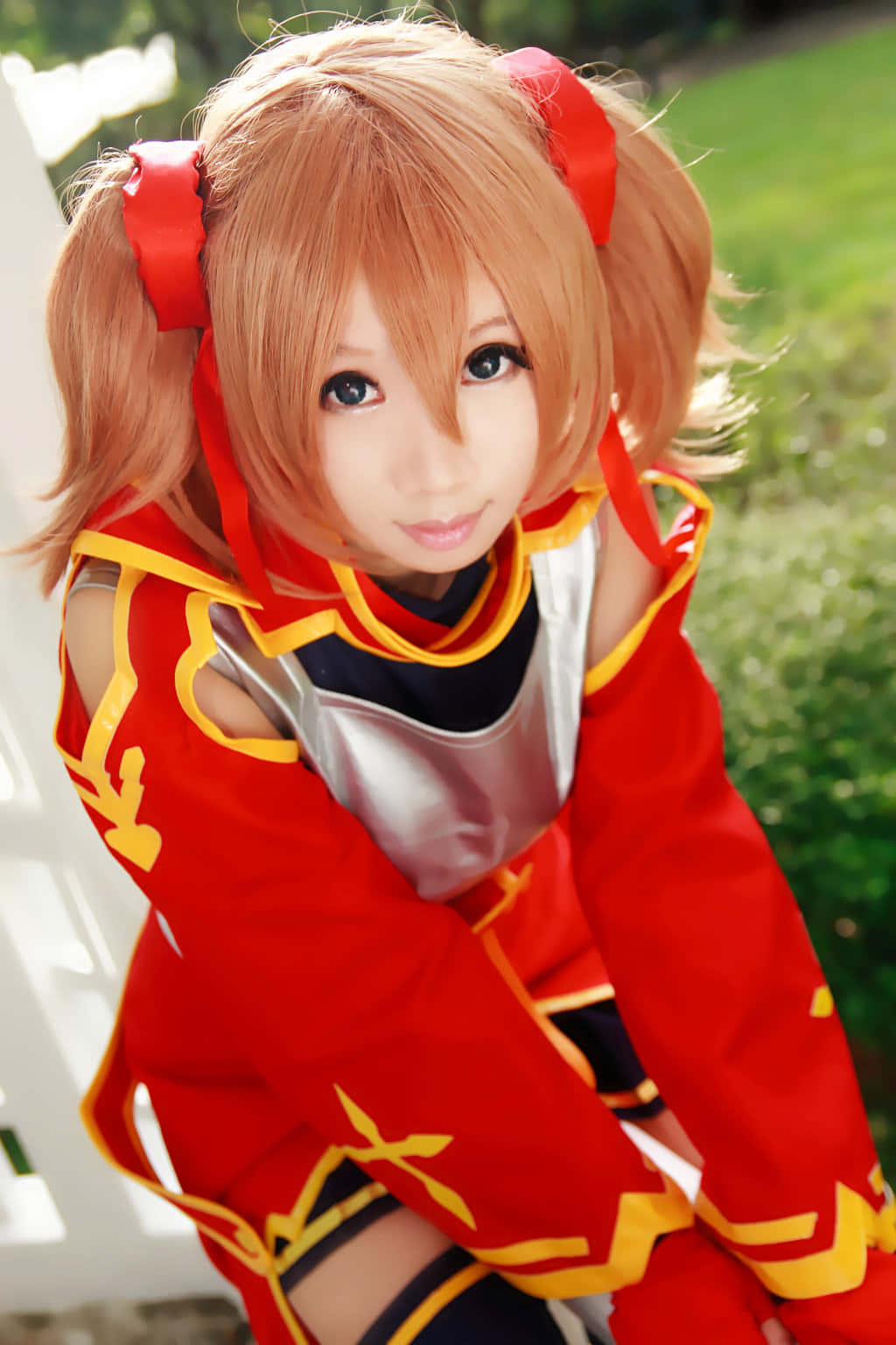 Sword Art Online Cosplay 桌布 壁紙 — 一位紮著橙色雙馬尾、繫著紅色絲帶的cosplayer，身穿鮮豔的紅金色服裝，在陽光明媚的綠色草坪上擺姿勢。