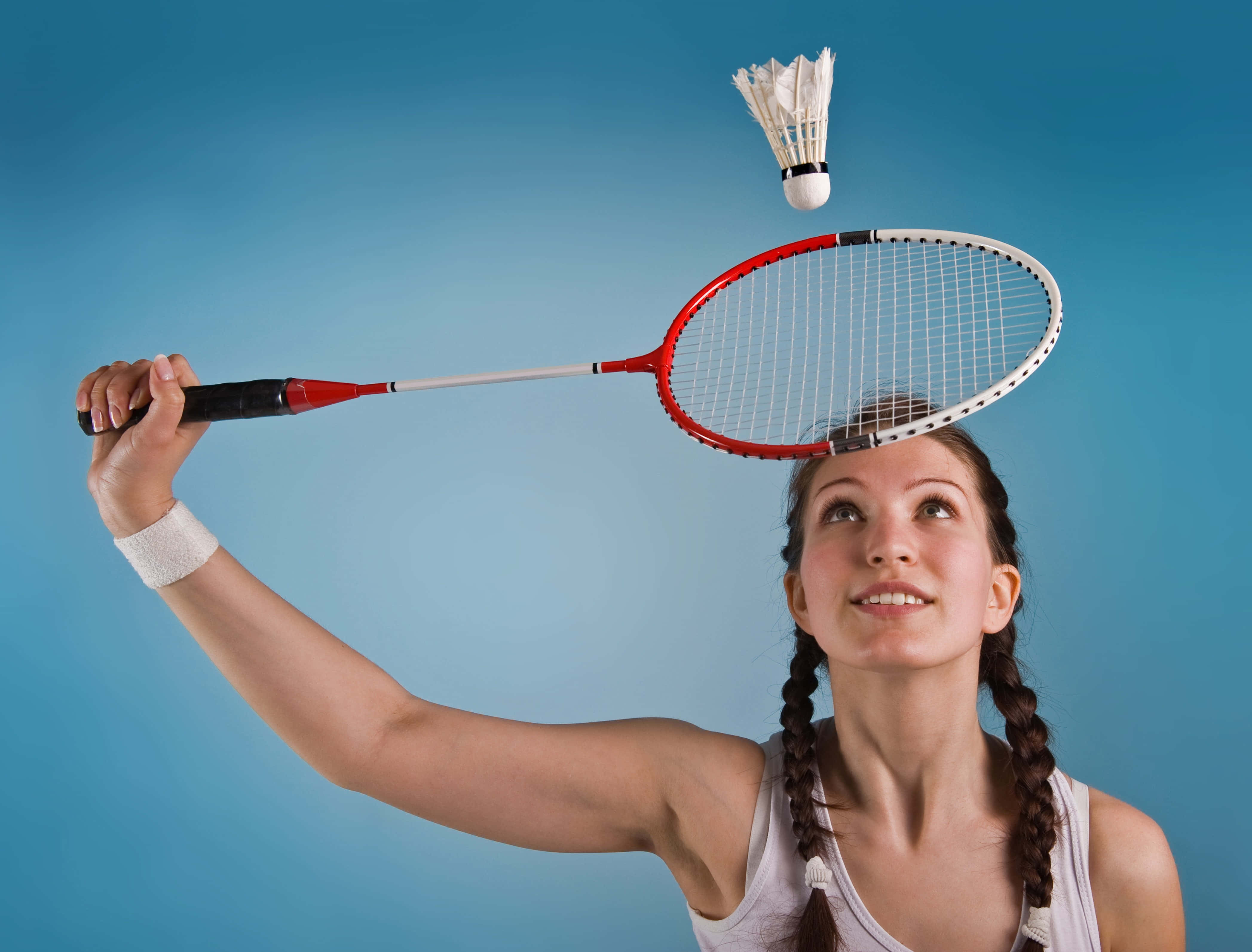 Badminton 桌布 壁紙 — 一位紮辮的年輕女性在純藍色攝影棚背景前平衡紅色羽毛球拍和羽毛球。
