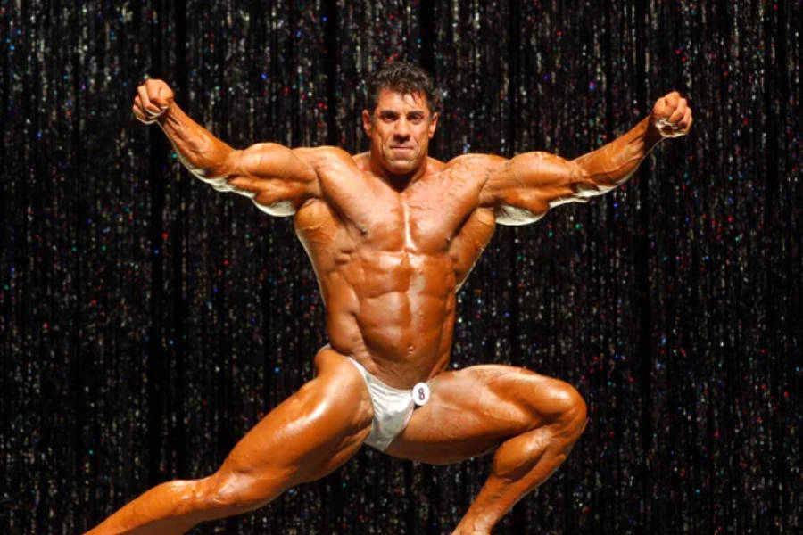 Exercise 桌布 壁紙 — 一位肌肉發達的健美運動員在閃爍的舞台燈光背景下擺出強而有力的姿勢。