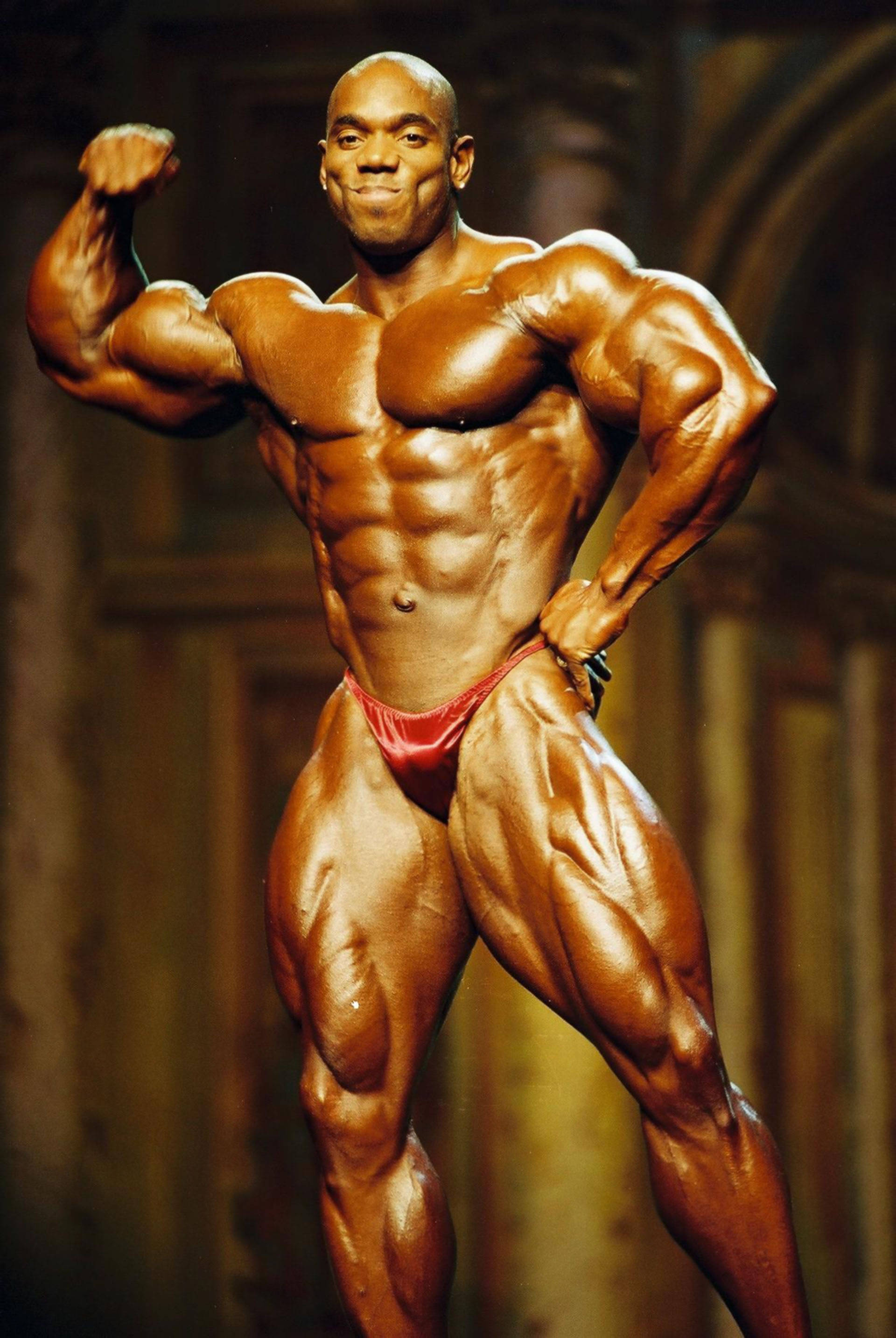 Funky Flex Wheeler 壁紙 — 一位肌肉發達的健美運動員穿著紅色比賽褲，在舞台燈光下展示他線條分明的體格。