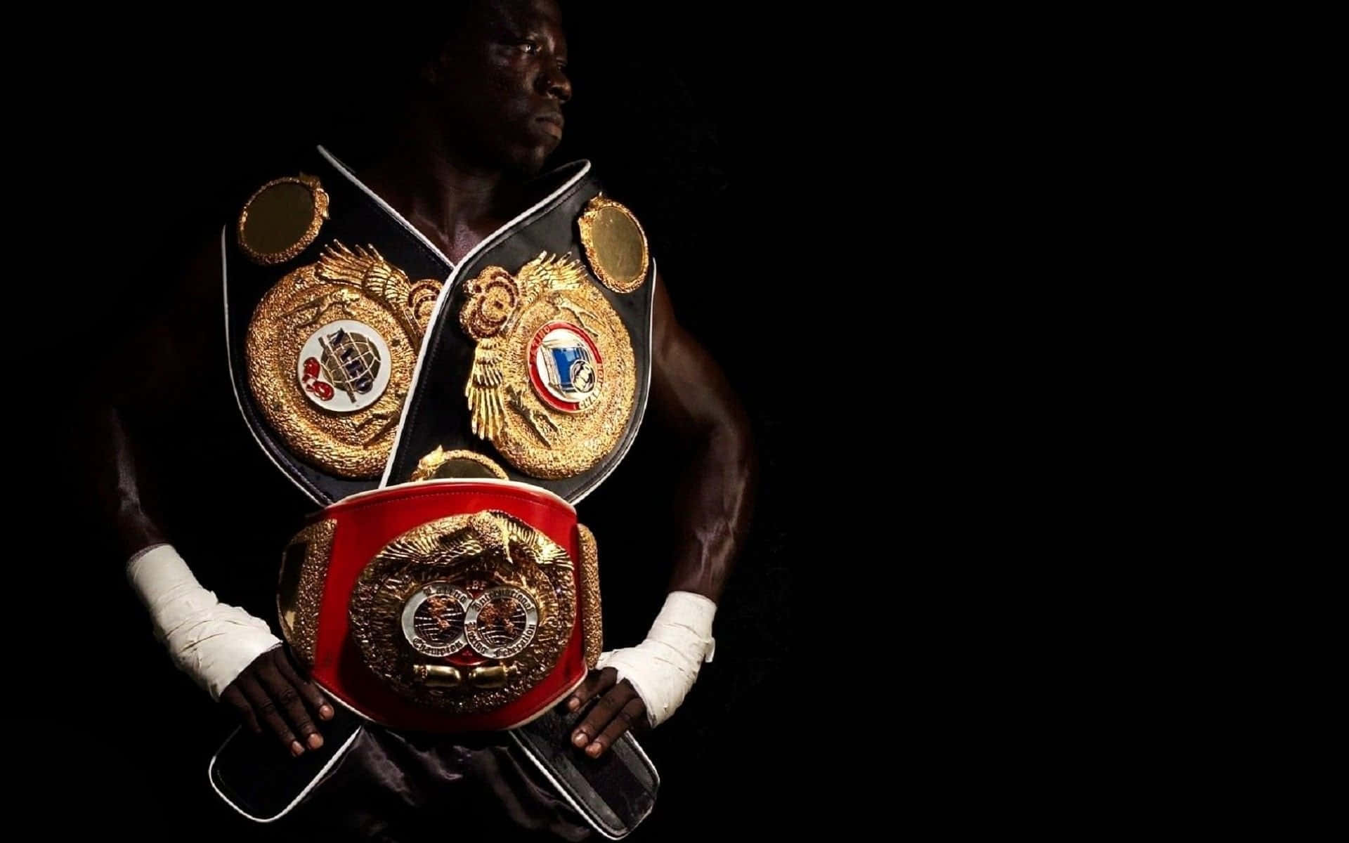 Boxing 桌布 壁紙 — 一位肌肉發達的拳擊手，纏著白色護手帶，在純黑背景前手持三條冠軍腰帶。