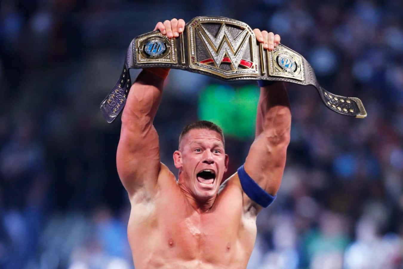 John Cena 桌布 壁紙 — 一位肌肉發達的摔角手在咆哮的體育館中勝利地將WWE冠軍腰帶高舉過頭。