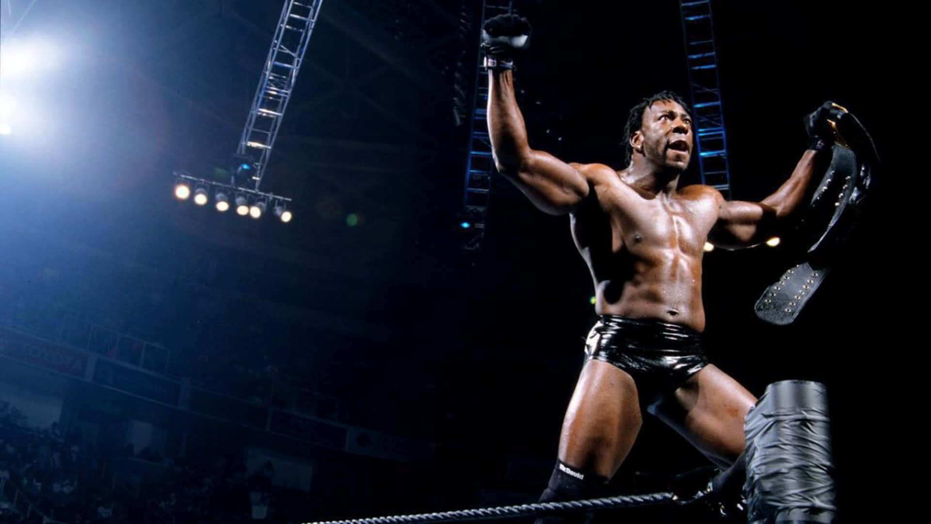 American Professional Wrestler Booker T 2002 Entrance 壁紙 — 一位肌肉發達的摔角手在場館燈光下，於明亮照明的擂台上勝利地高舉雙臂和冠軍腰帶。