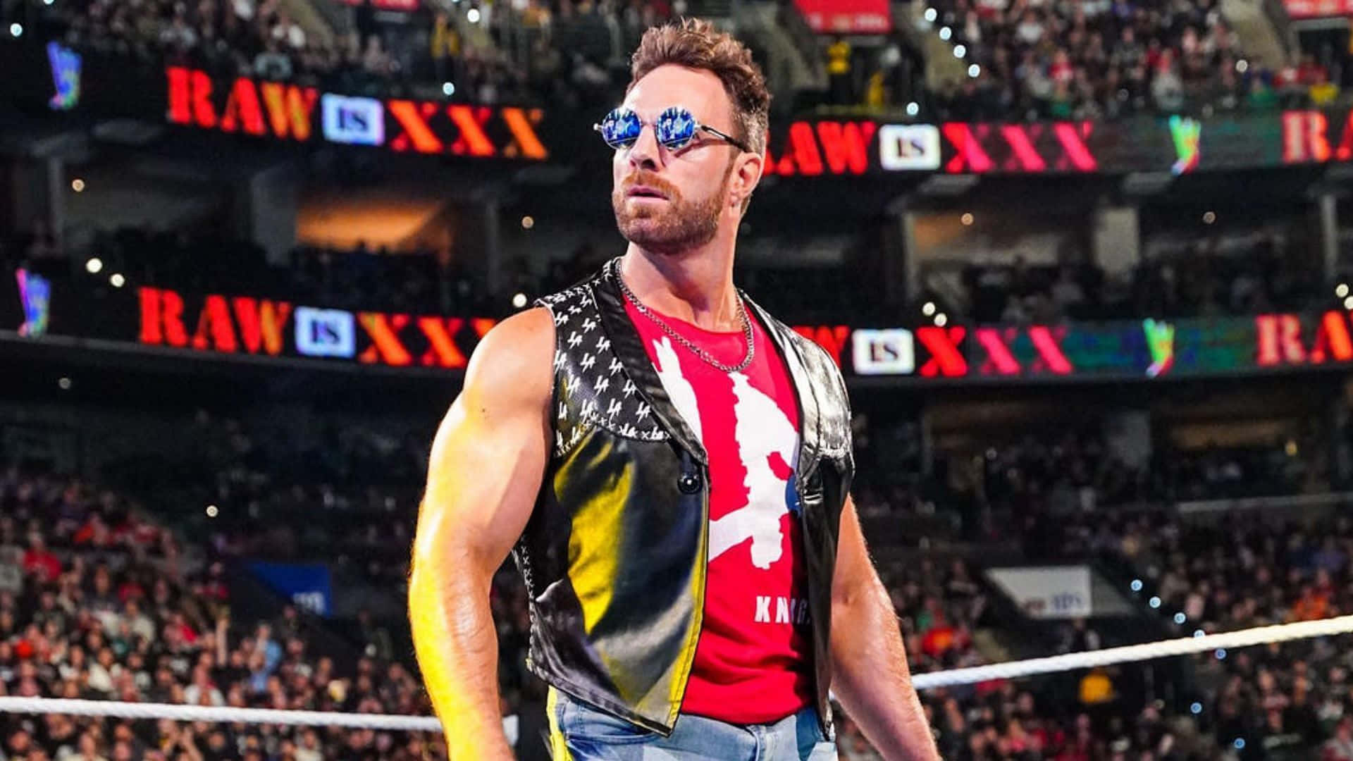 La Knight WWE Raw 30 壁紙 — 一位肌肉發達的摔角手戴着太陽眼鏡和皮背心，自信地站在摔角擂台上，身後是座無虛席的場館。