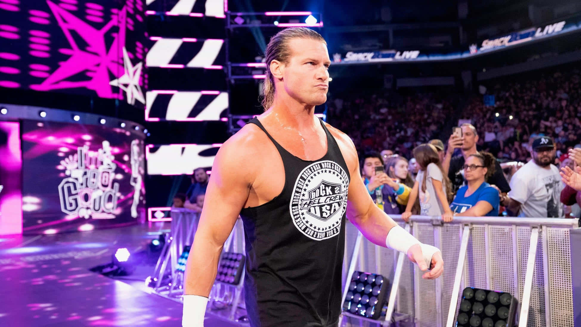 Dolph Ziggler WWE Two-time Champion 壁紙 — 一位肌肉發達的摔角手穿著黑色背心，自信地走過一個燈光璀璨、紫色燈光與歡呼粉絲環繞的競技場。