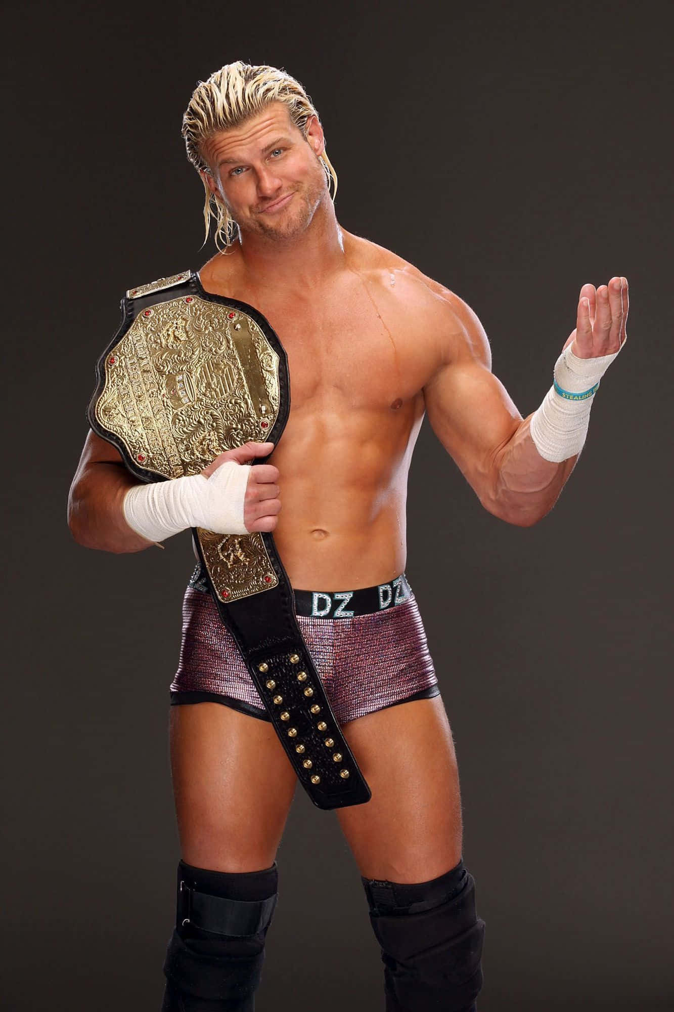 Dolph Ziggler WWE Champion 壁紙 — 一位肌肉發達的金髮摔角手穿著閃亮短褲，自信地擺姿勢，手持冠軍腰帶，背景是黑暗的攝影棚。
