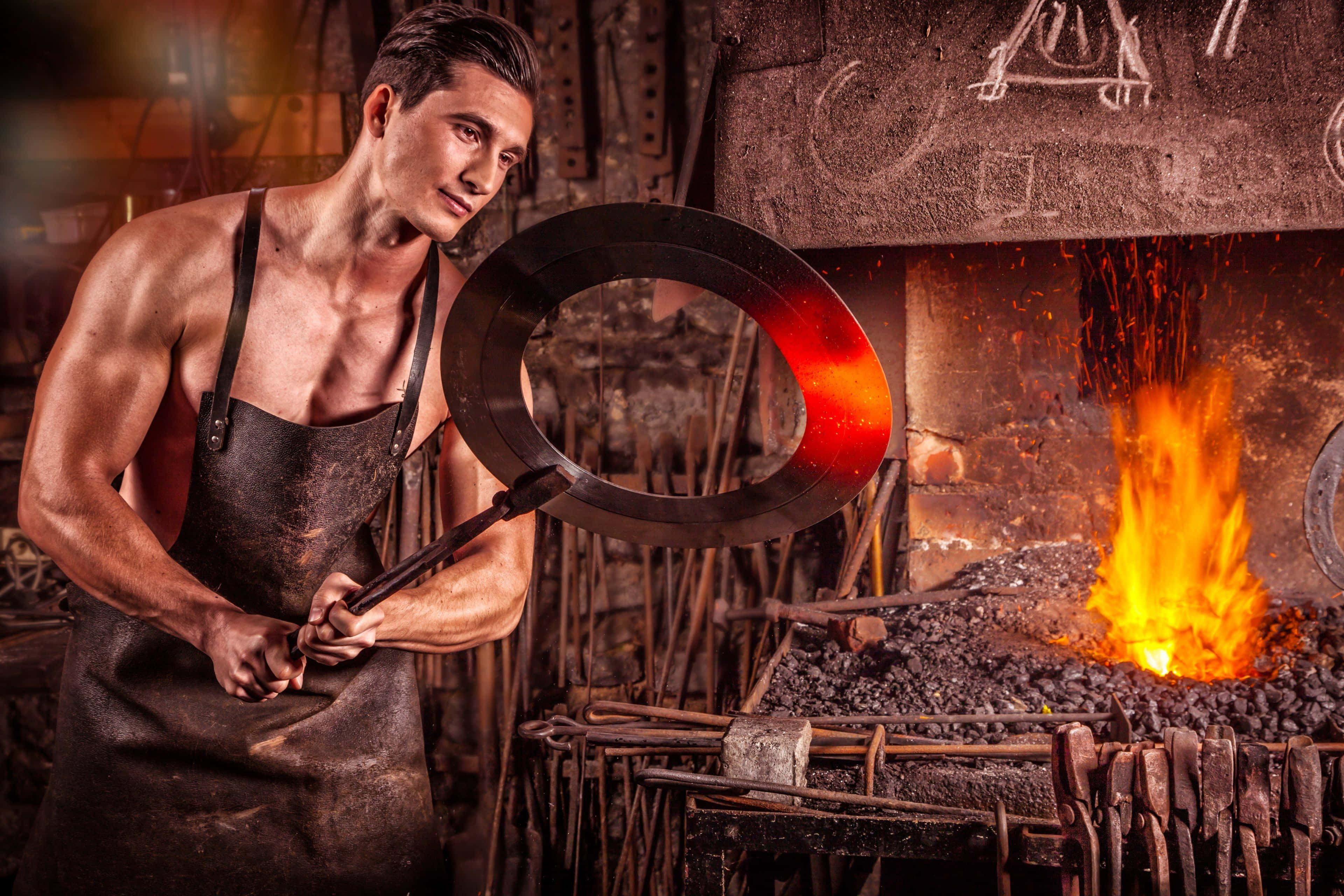 Blacksmith 桌布 壁紙 — 一位肌肉發達的鐵匠站在鄉村風格工坊的火爐前，手持一個熾熱的金屬環。