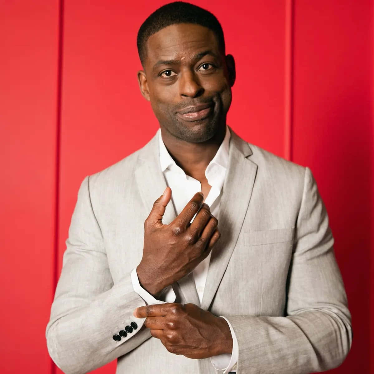 Sterling K Brown 桌布 壁紙 — 一位自信嘅男人著住淺灰色西裝，喺大膽嘅紅色攝影棚背景前調整袖口。