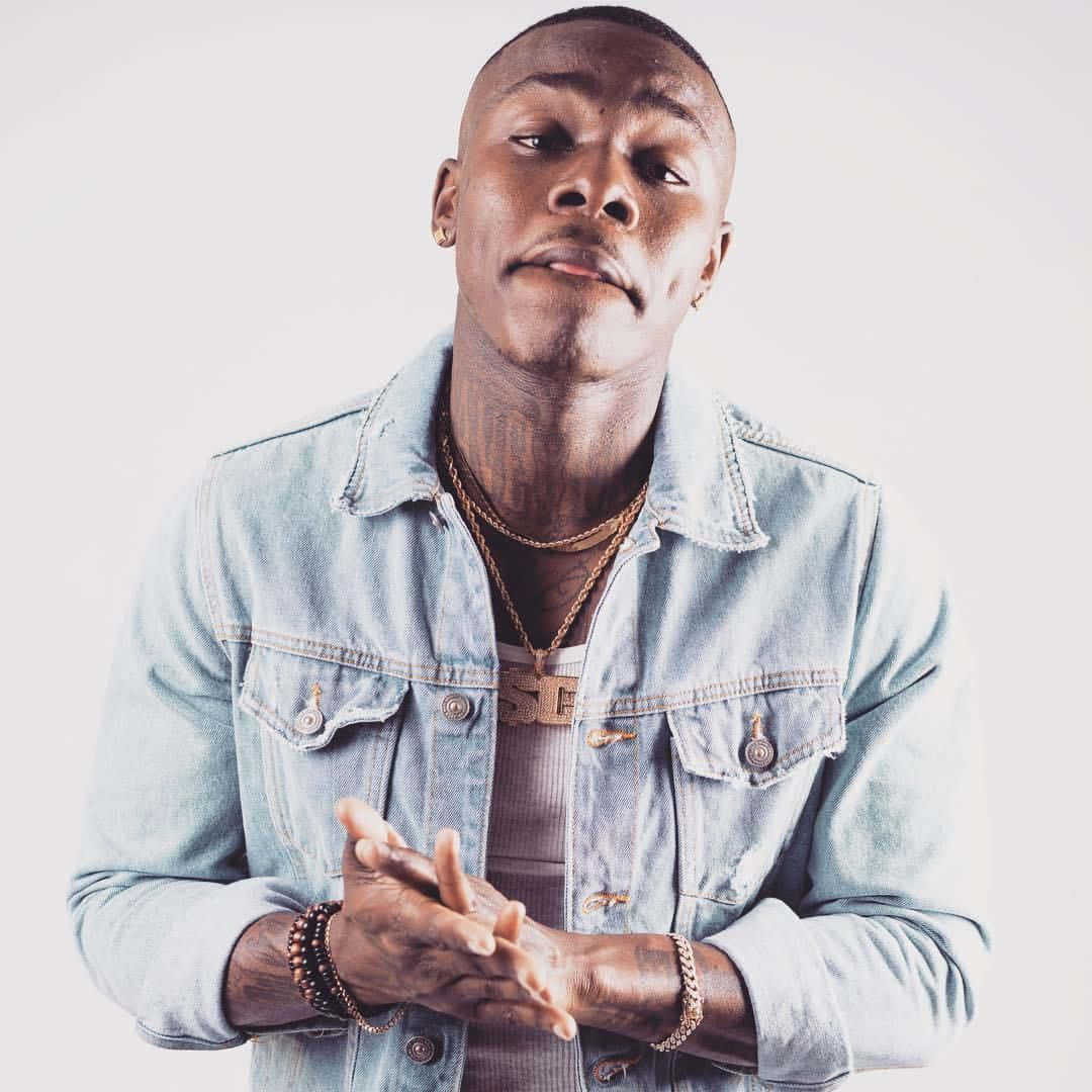 Dababy 桌布 壁紙 — 一位自信嘅男人著住淺藍色牛仔褸，喺純白背景前交叉雙手擺甫士。