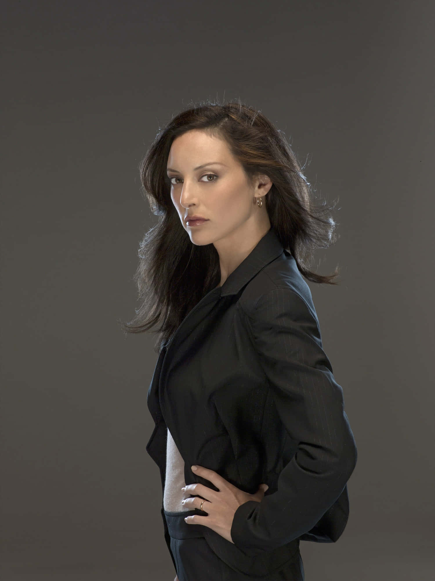 paget brewster 桌布 壁紙 — 一位自信的女性穿著黑色西裝外套，在柔和的灰色背景前直視鏡頭。