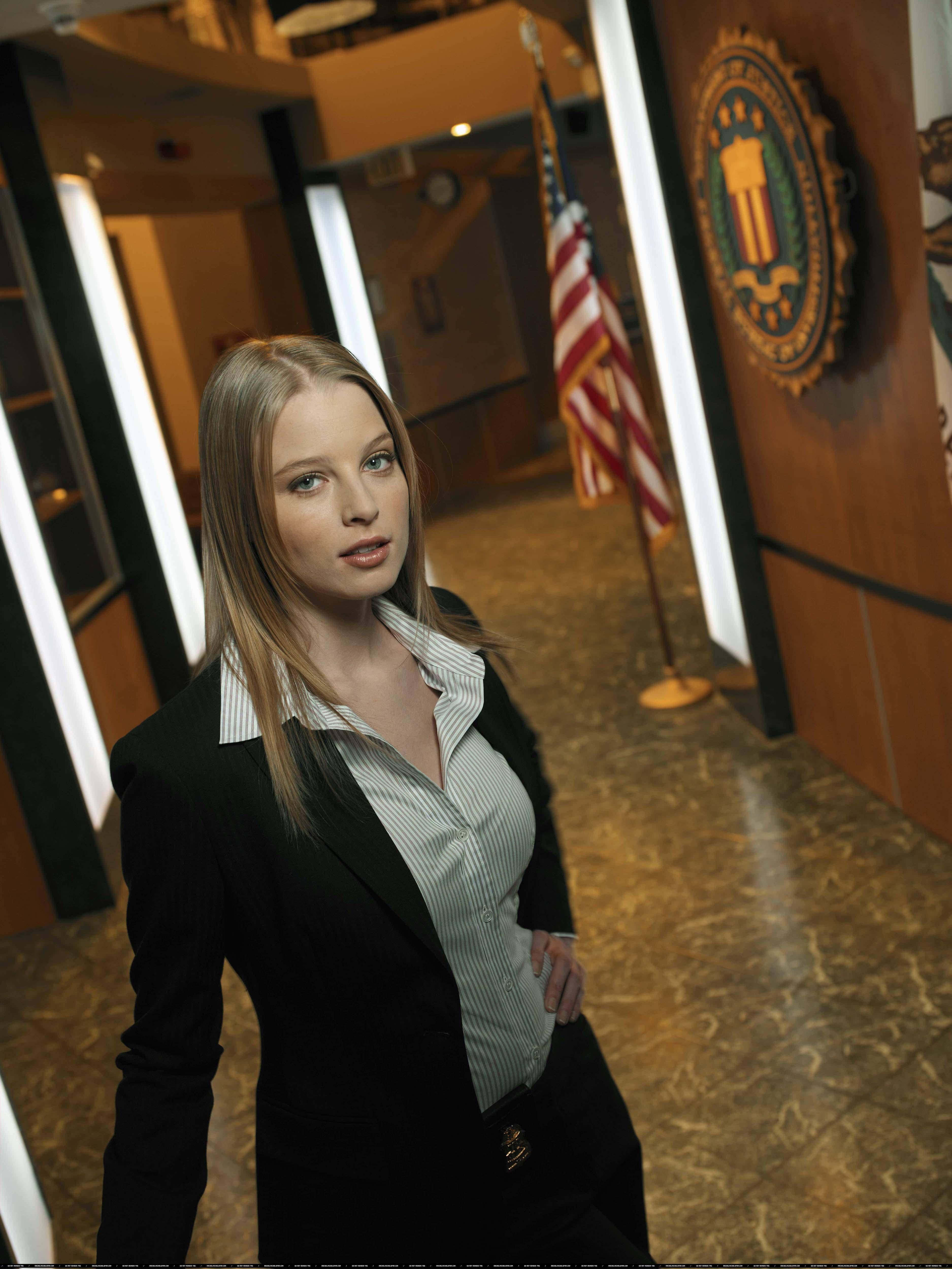 rachel nichols 桌布 壁紙 — 一位自信的女性身穿黑色西裝，站在政府走廊，身後有美國國旗和官方印章。