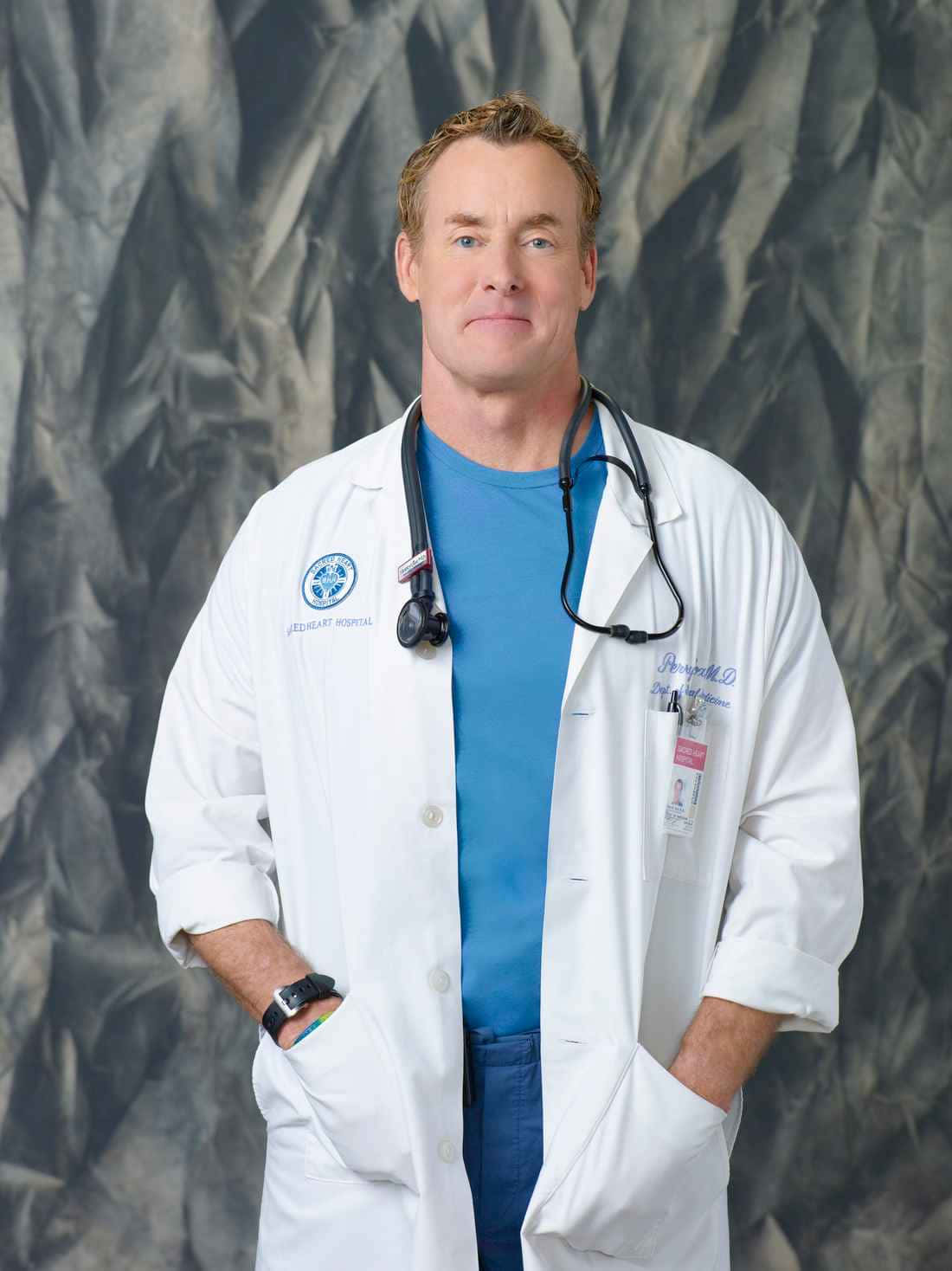 John C. Mcginley 桌布 壁紙 — 一位自信的男醫生穿著白色實驗室外套和聽診器，雙手插袋，站在有紋理的灰色背景前。