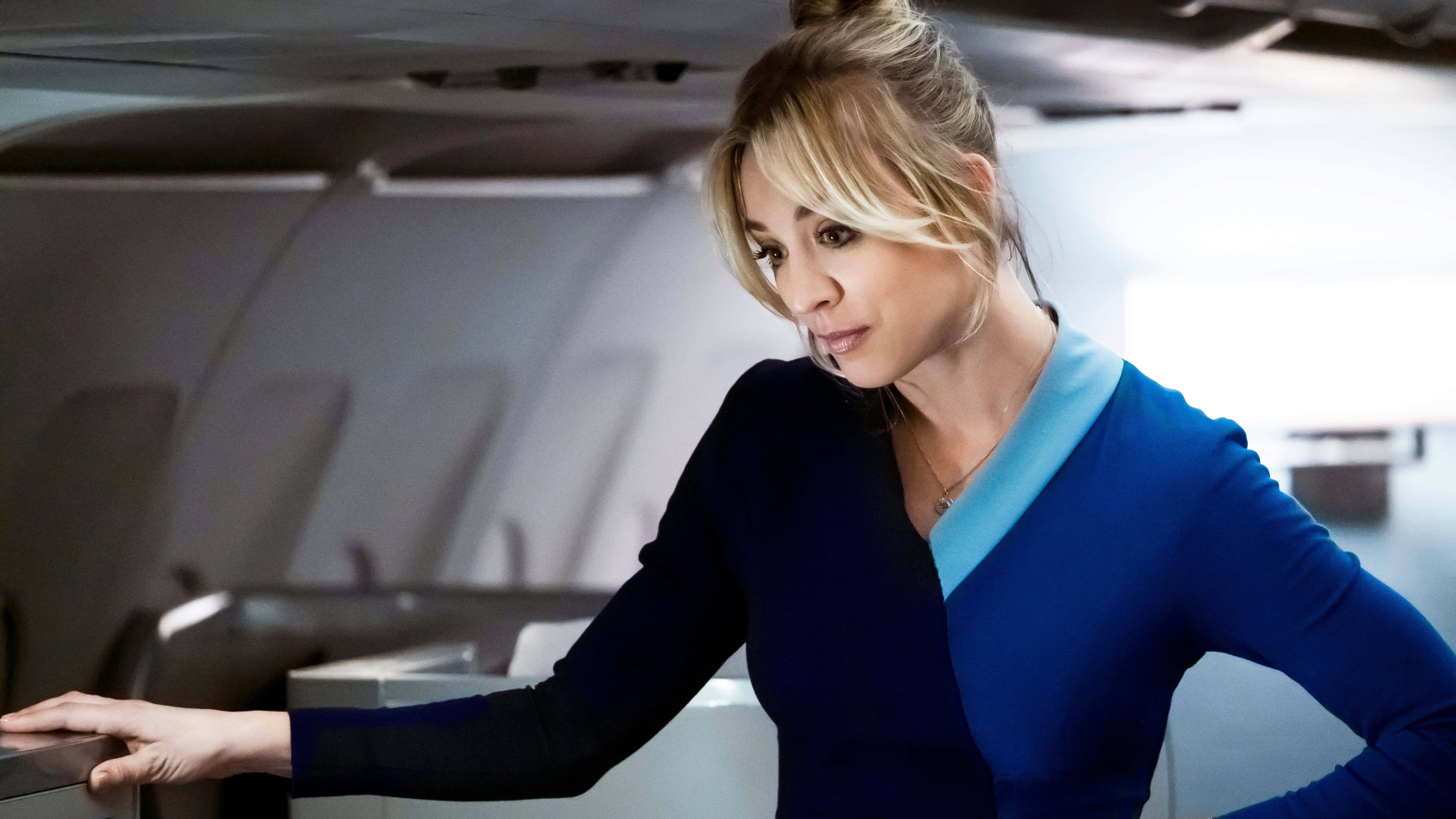 Flight Attendant 桌布 壁紙 — 一位自信的空中服務員穿著藍色制服，在柔和燈光的飛機艙內倚靠著。