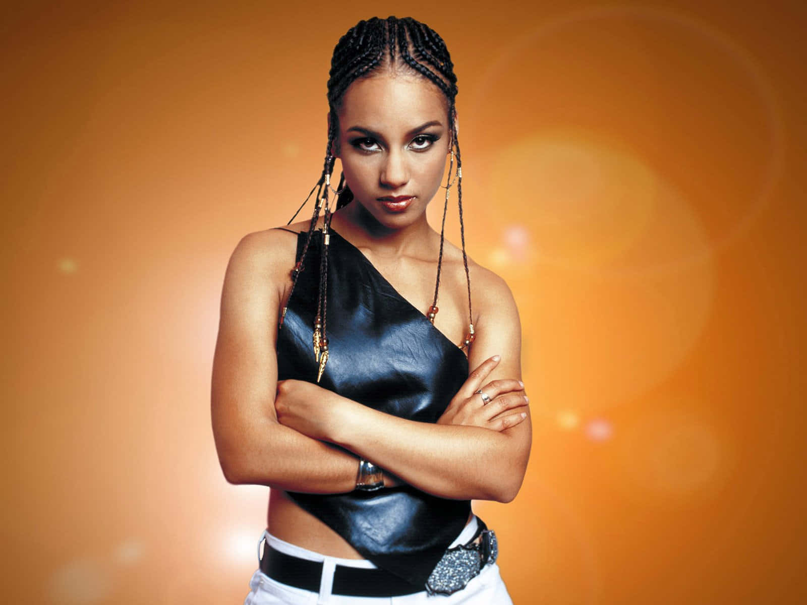 Alicia Keys 桌布 壁紙 — 一位自信的辮髮女性穿著黑色皮革上衣和白色褲子，背景是溫暖的橙色漸變和鏡頭光暈。