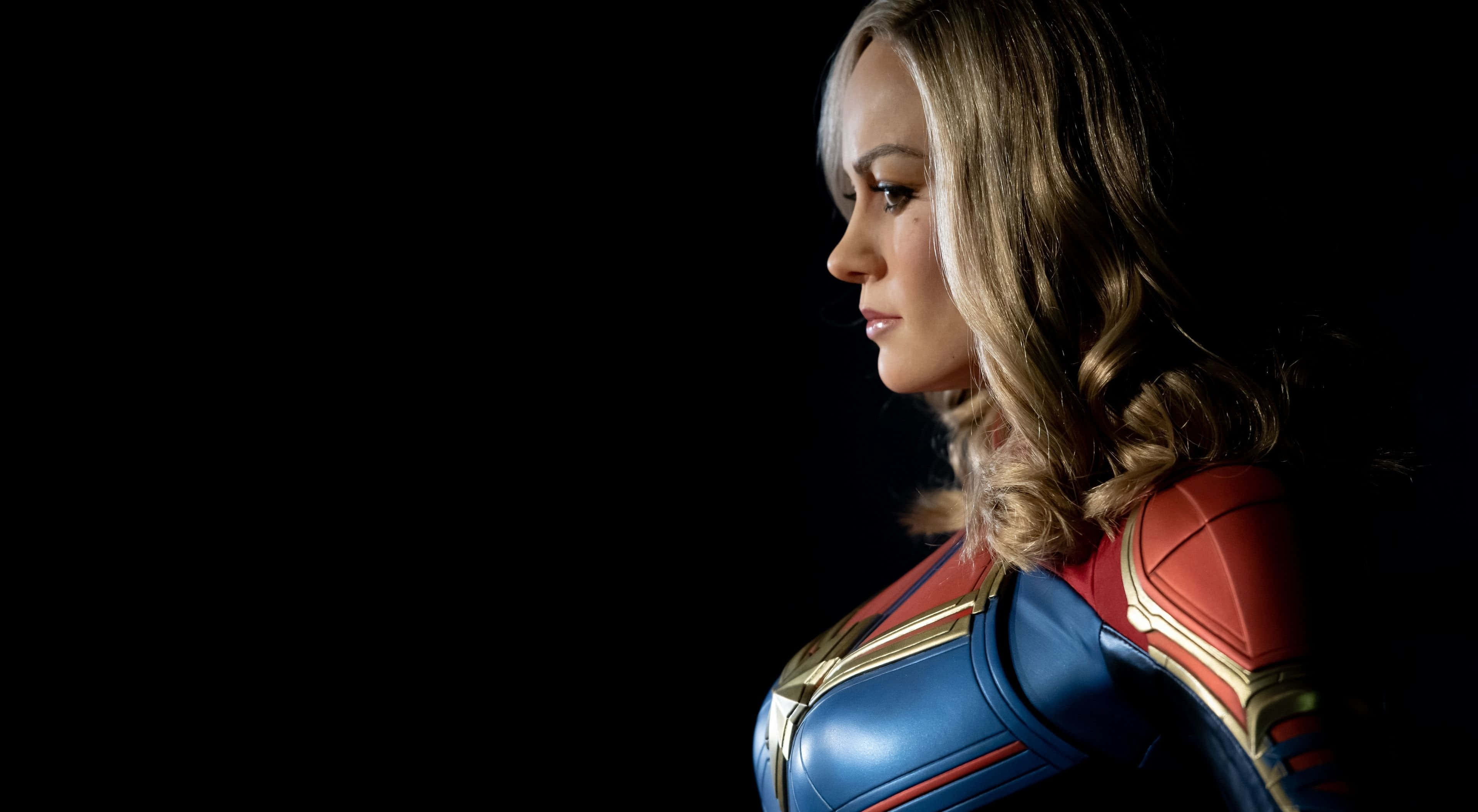 4K Marvel 壁紙 桌布 壁紙 — 一位英勇的女性超級英雄身穿紅、藍、金色戰衣，在純黑背景前側面站立。