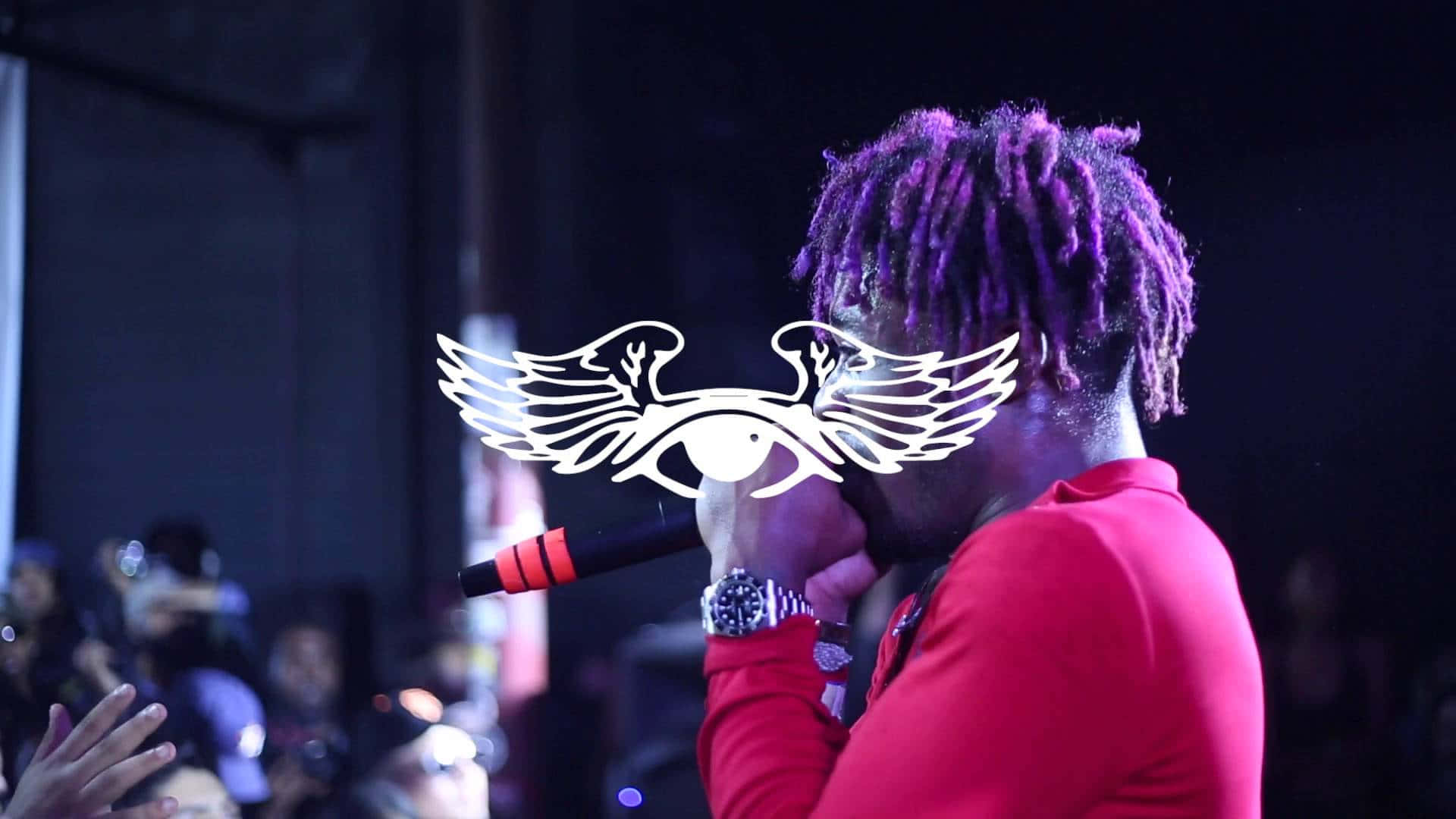 Lil Uzi Vert 桌布 壁紙 — 一位表演者留著紫色辮子，在舞台燈光下對著麥克風唱歌，並帶有發光的有翼眼睛標誌疊加。