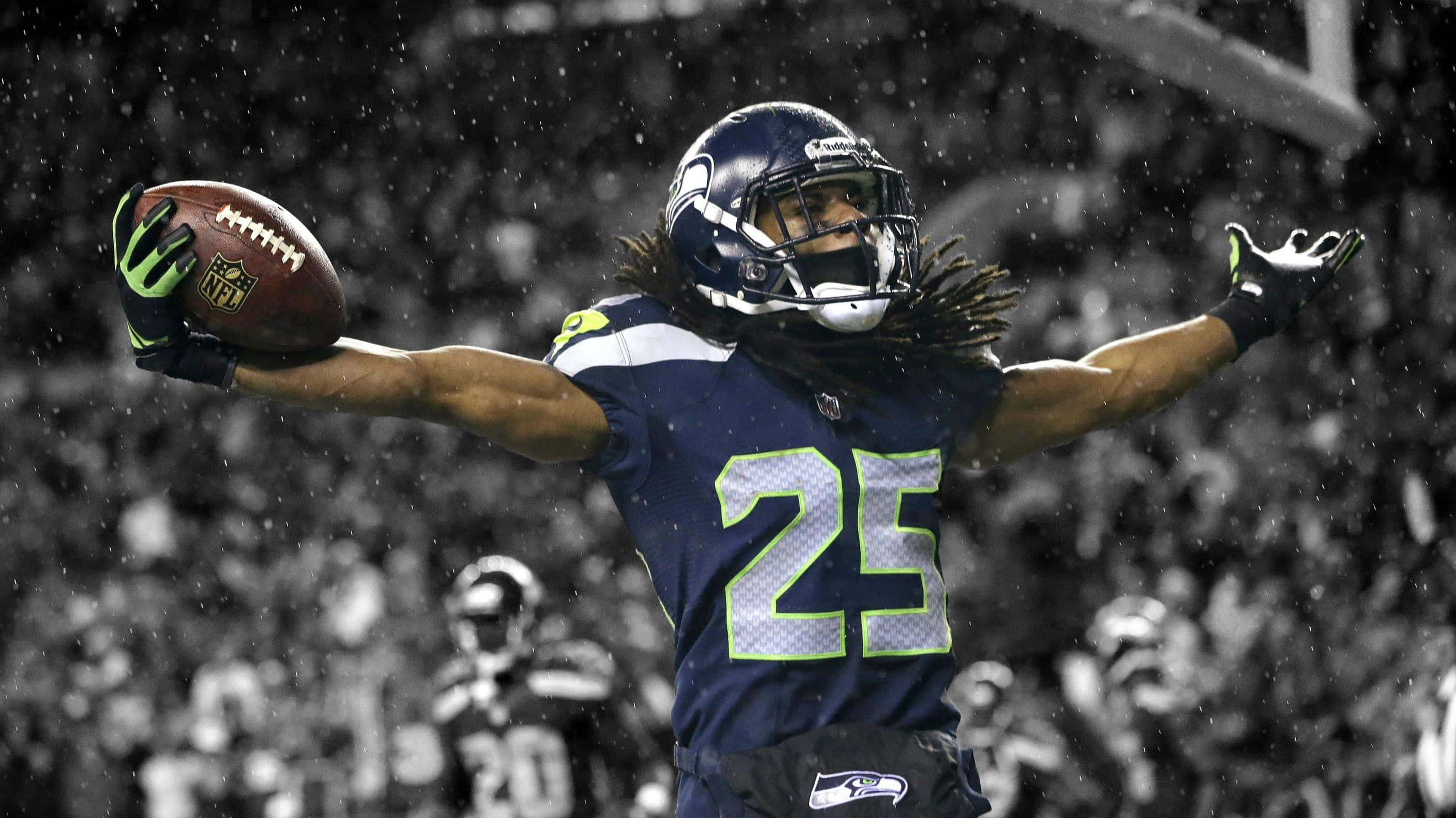 NFL 桌布 壁紙 — 一位西雅圖海鷹隊的美式足球員在雨中張開雙臂，高舉球，慶祝勝利。