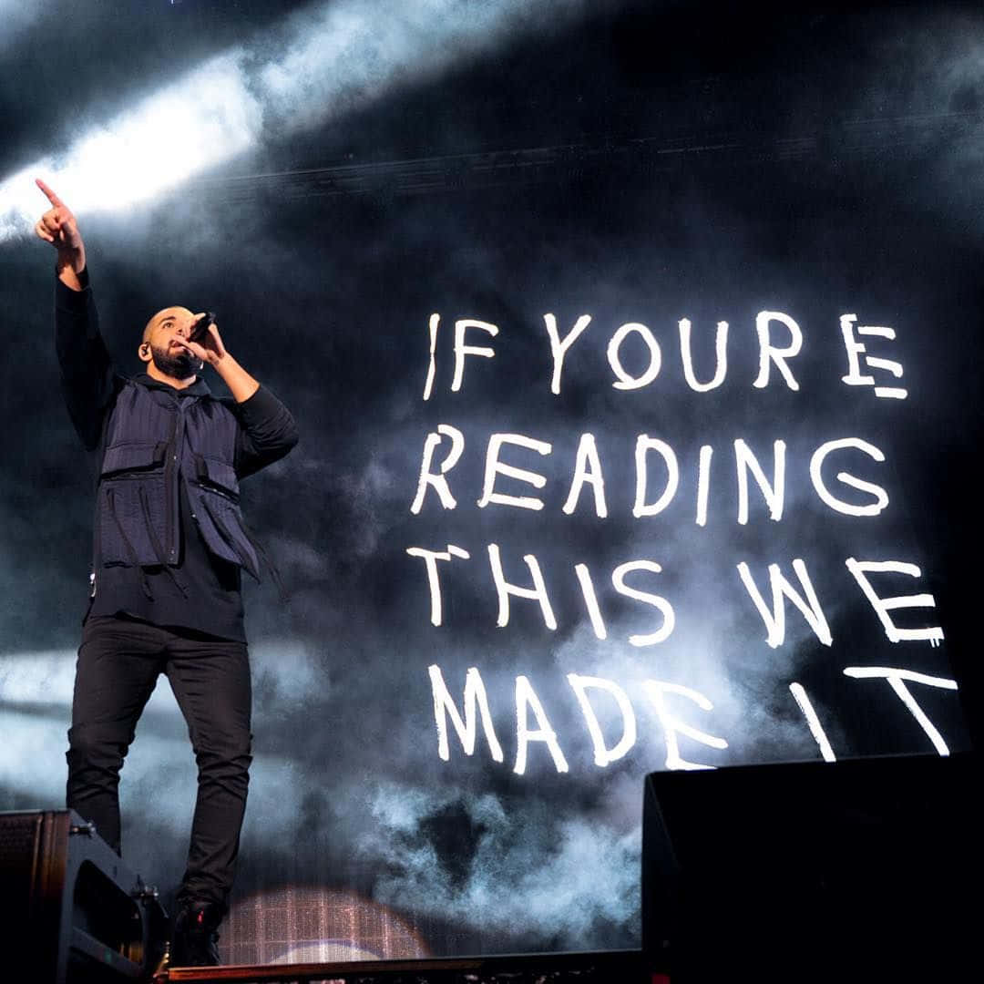 Drake 桌布 壁紙 — 一位說唱歌手在明亮的燈光、煙霧和一個顯示「if youre reading this we made it」的大屏幕下於舞台上表演。