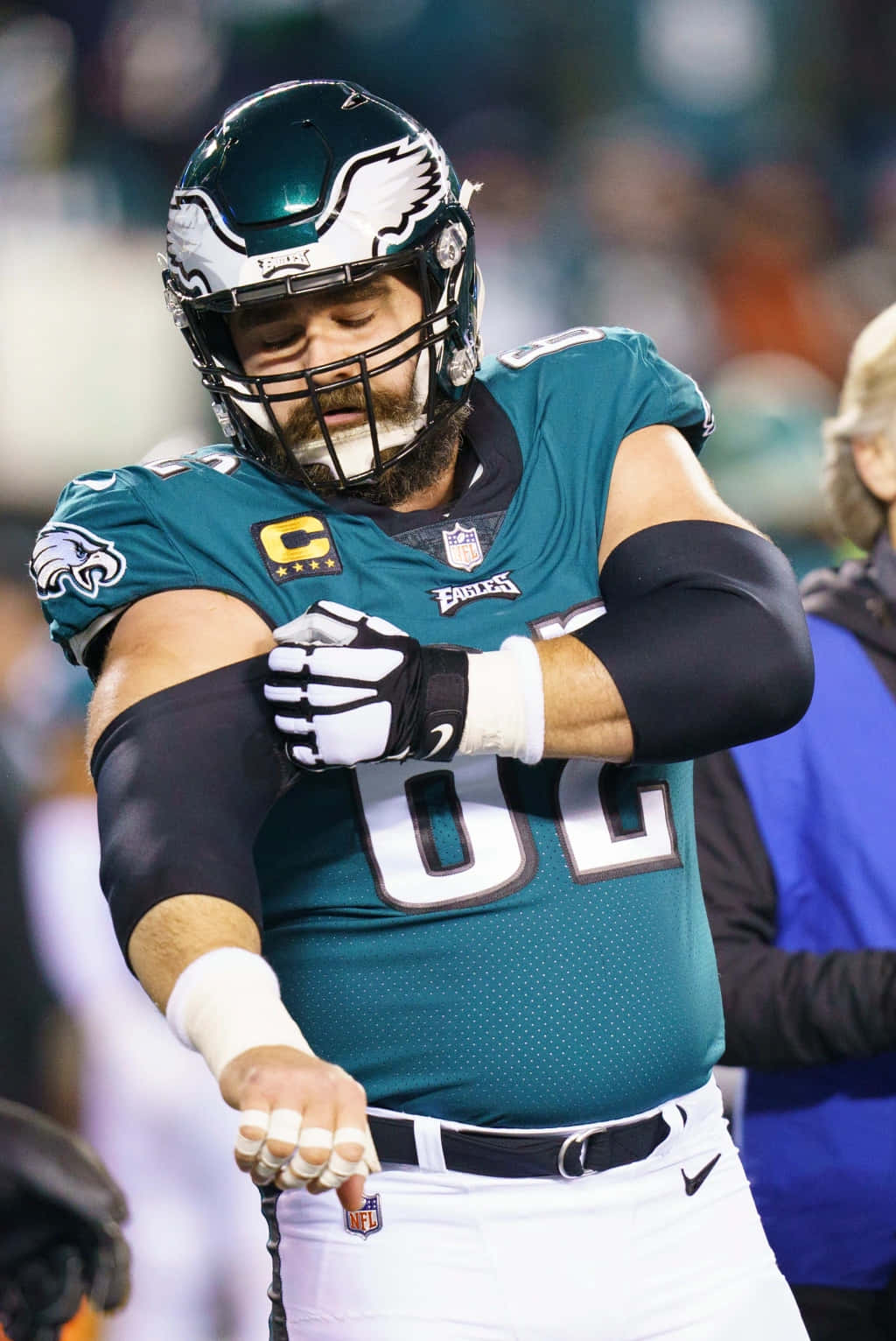 Jason Kelce 桌布 壁紙 — 一位費城老鷹隊的美式足球員穿著青綠色制服，在體育館燈光下的比賽中調整手套。