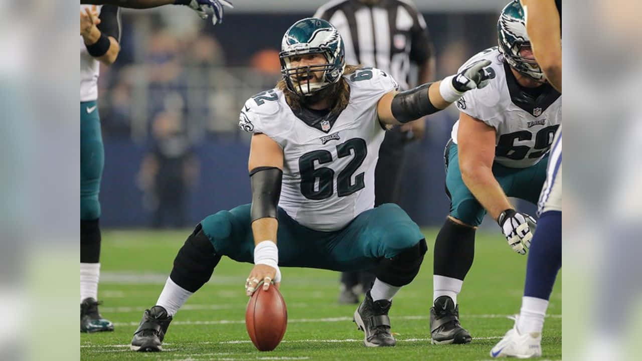 Jason Kelce 桌布 壁紙 — 一位費城老鷹隊的進攻鋒線球員身穿白色和藍綠色球衣，在夜間比賽中低蹲著拿著橄欖球準備開球。
