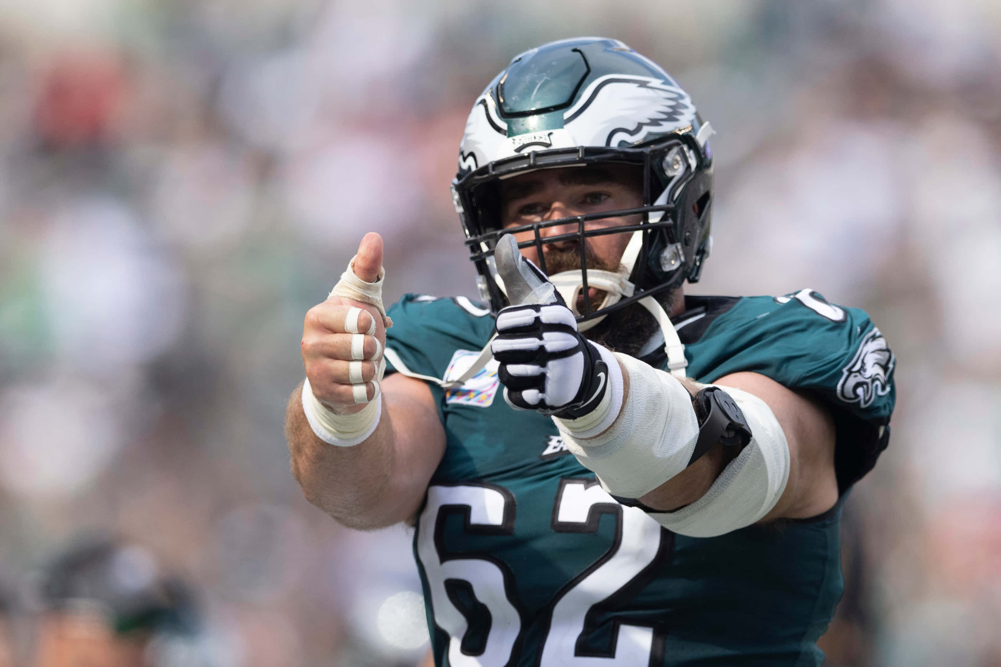 Jason Kelce 桌布 壁紙 — 一位費城老鷹隊身穿綠色球衣62號的美式足球員在陽光明媚的比賽中自信地豎起雙拇指。