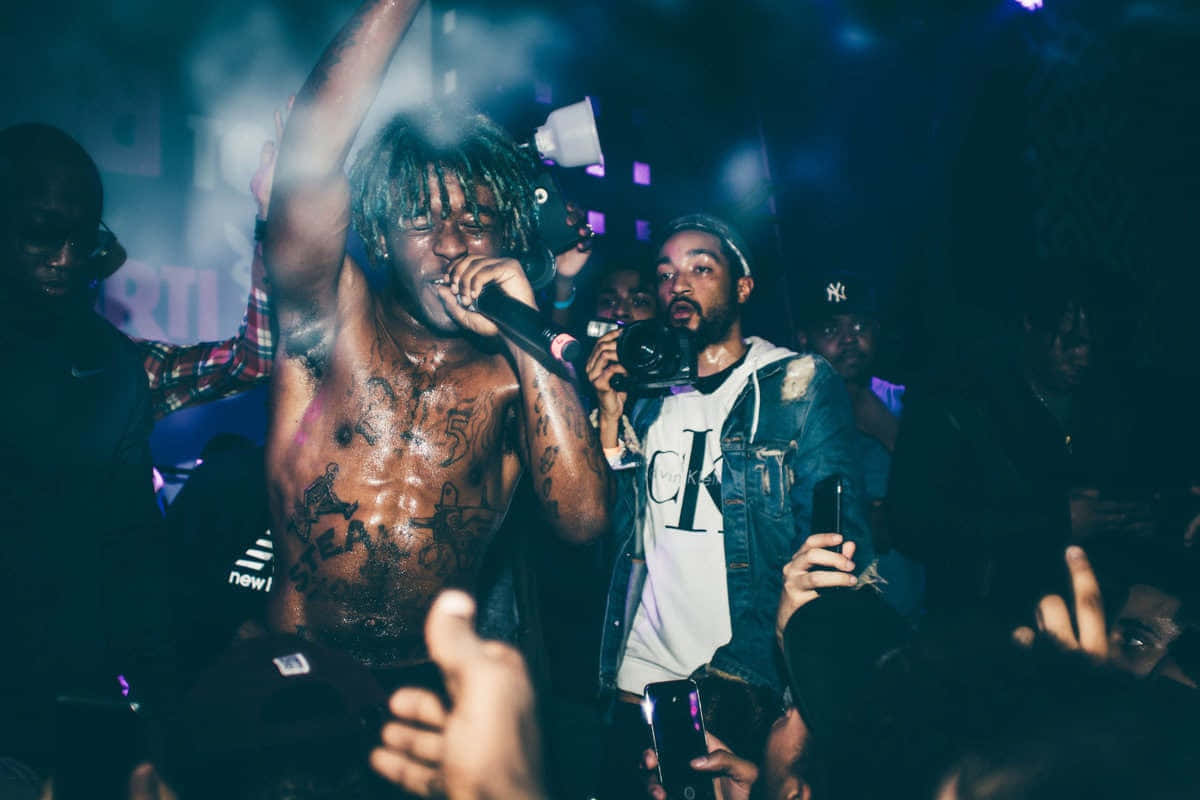 Lil Uzi Vert 桌布 壁紙 — 一位赤裸上身、紋身的說唱歌手在煙霧繚繞的藍色舞台燈光下，對著麥克風激情表演，觀眾投入其中。
