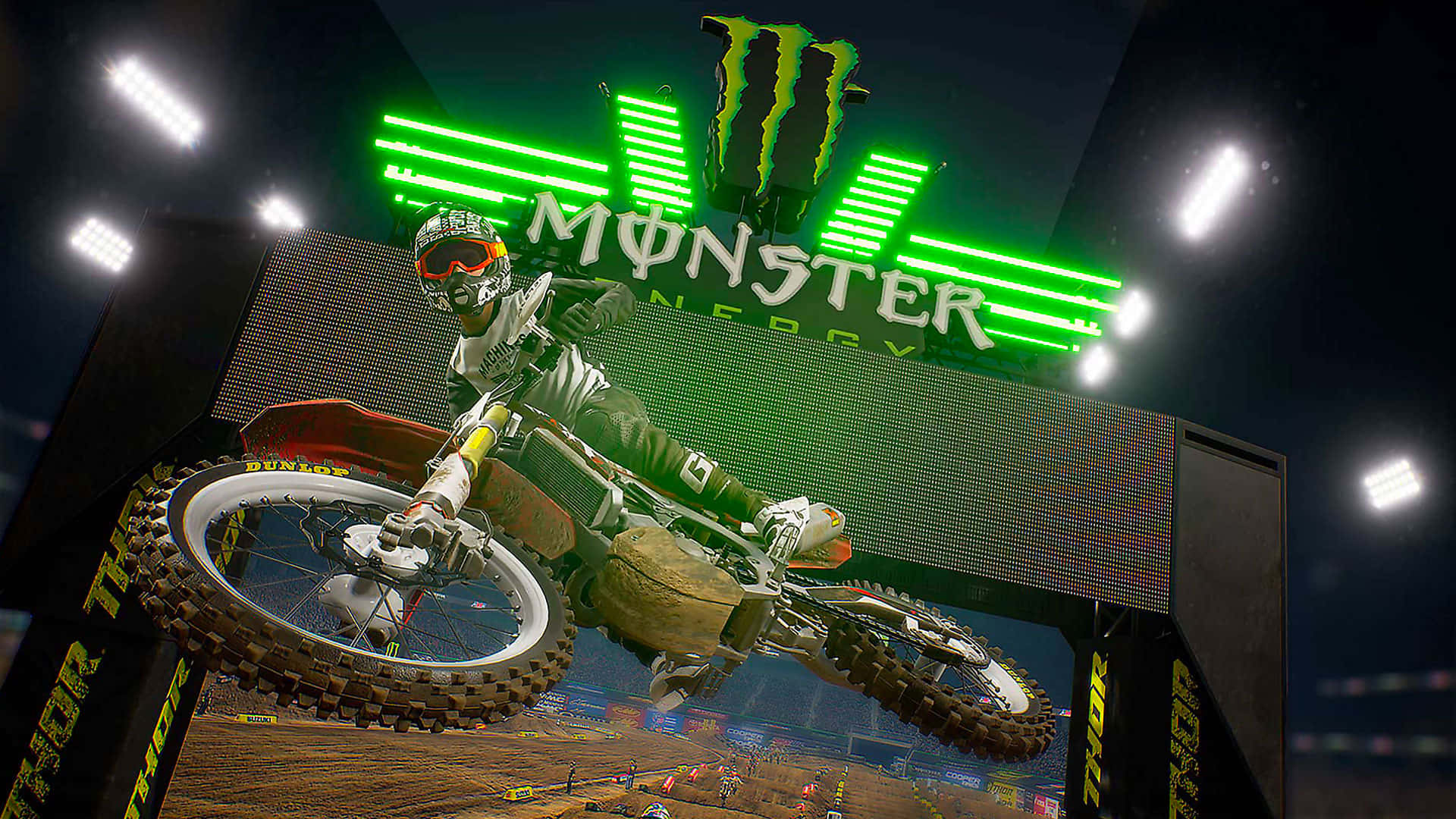 Monster Energy 桌布 壁紙 — 一位越野電單車手在夜間體育館內，於發光的綠色Monster Energy標誌下飛翔。