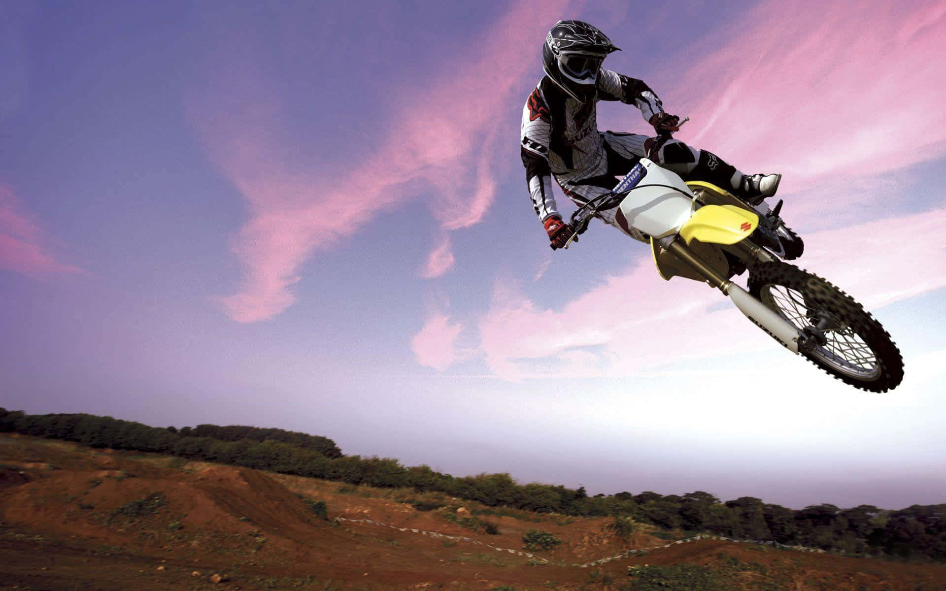 Motocross 桌布 壁紙 — 一位越野電單車手在崎嶇的泥地上方，飛越充滿活力的粉紅與紫色暮色天空。