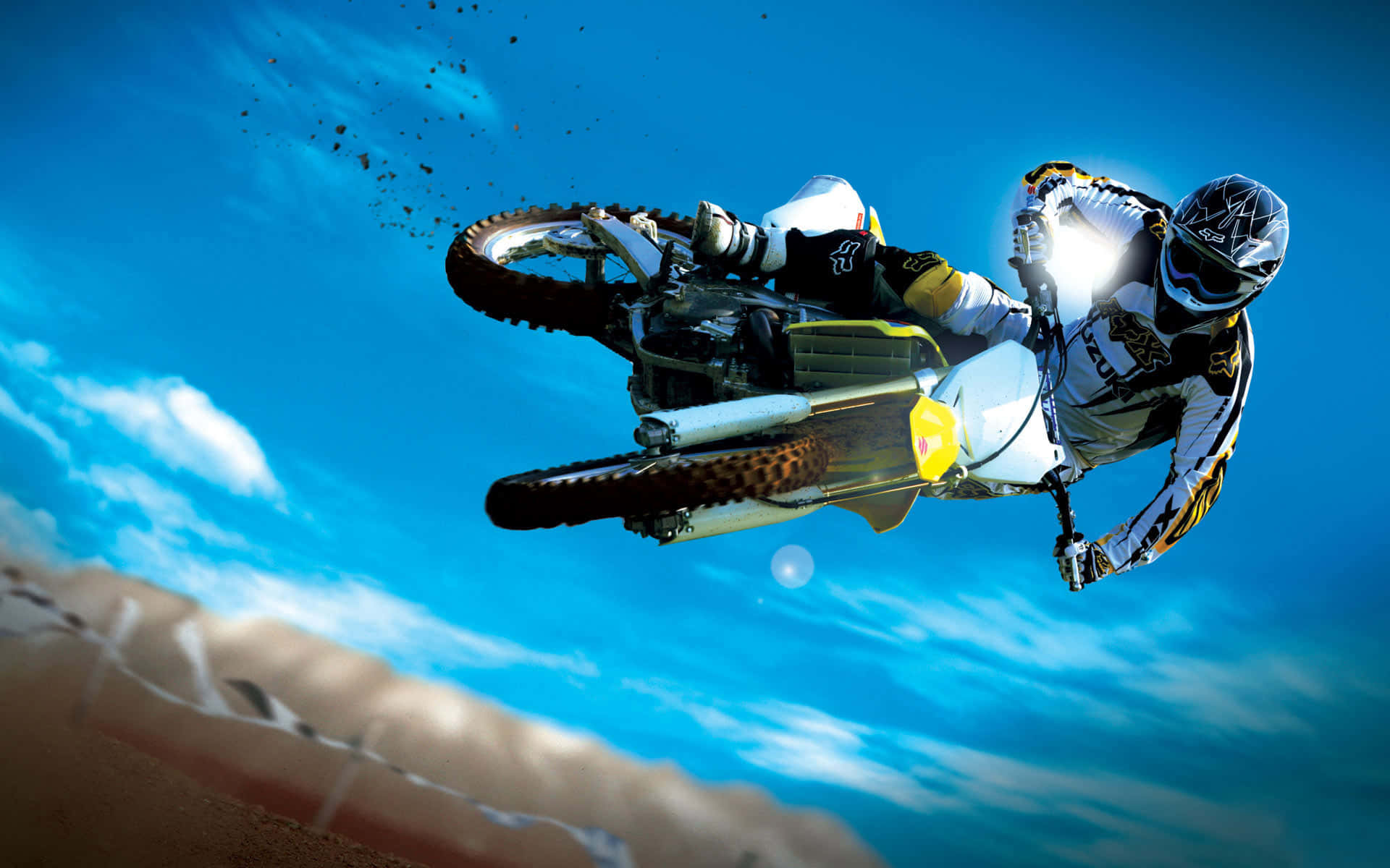 Motocross 桌布 壁紙 — 一位越野電單車手在泥地電單車上翱翔於空中，背景是湛藍的天空和散落的雲朵。