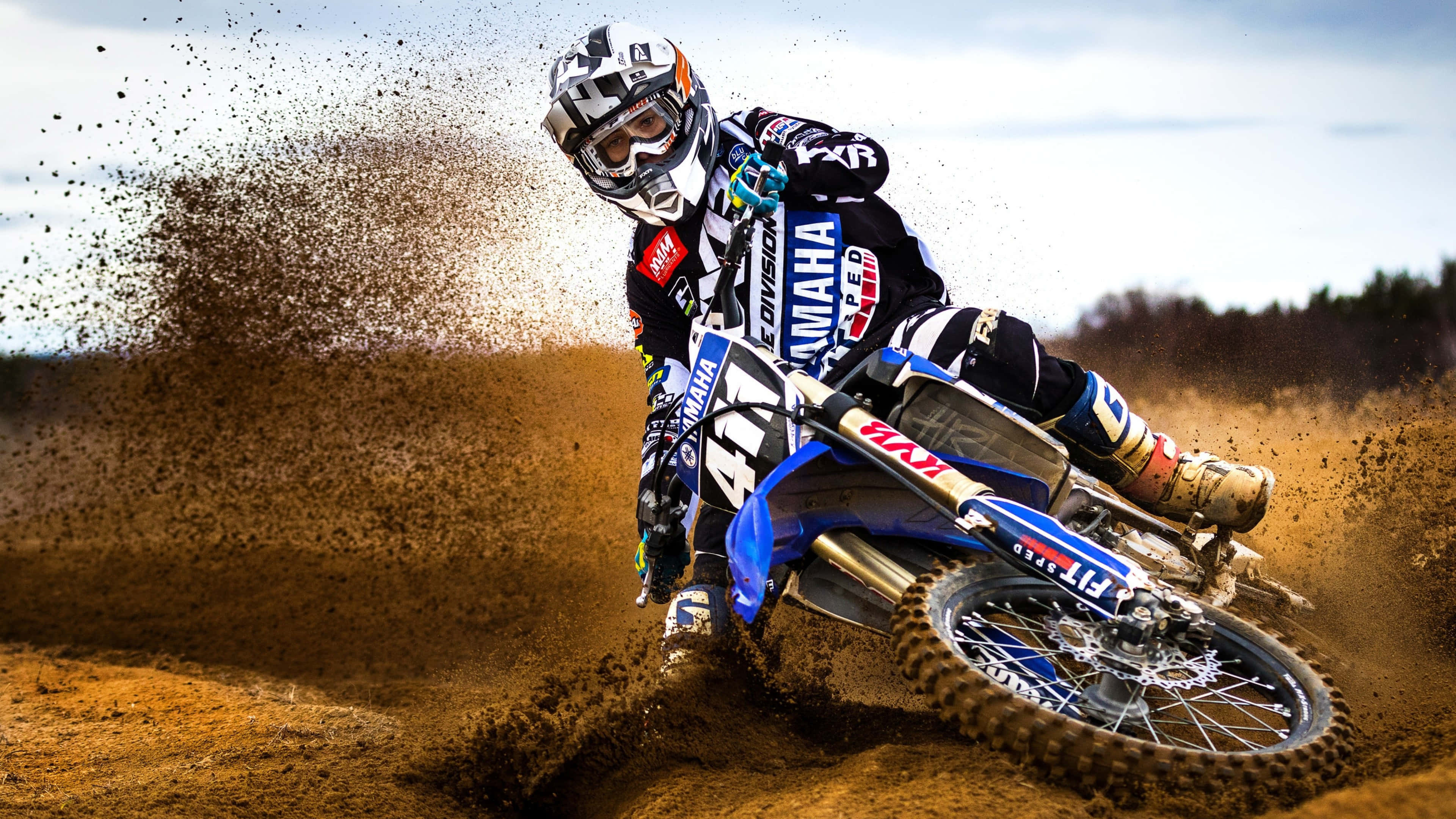 Motocross 桌布 壁紙 — 一位越野電單車手在藍色Yamaha電單車上傾斜入彎，在陽光明媚的戶外賽道上揚起泥土。