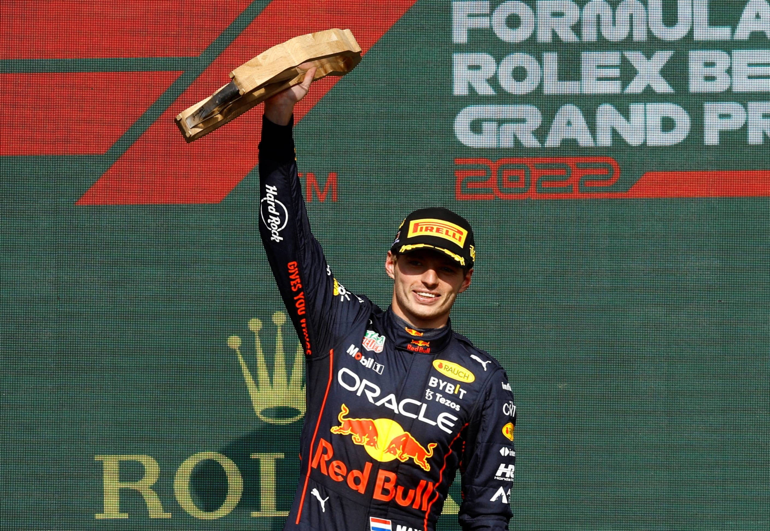 Trophy 桌布 壁紙 — 一位身穿Red Bull賽車服的F1車手在2022年勞力士大獎賽的頒獎台上高舉獎盃慶祝勝利。