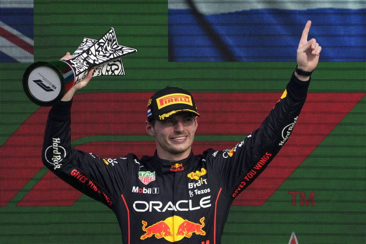 Verstappen 桌布 壁紙 — 一位身穿Red Bull賽車服的F1車手在頒獎台上慶祝，手持獎盃並指向天空。