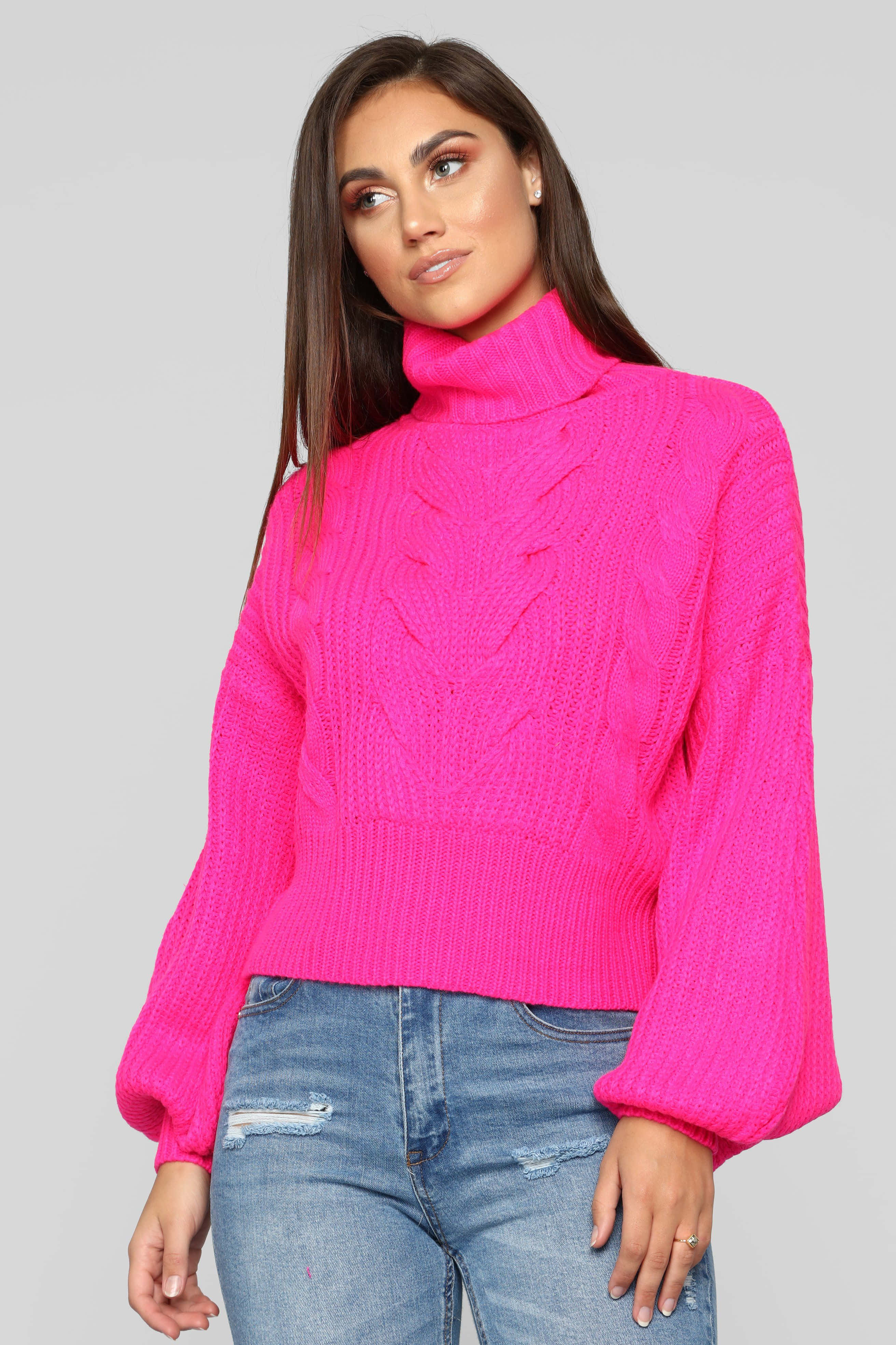 Pink Sweater 桌布 壁紙 — 一位身穿亮粉紅色麻花高領毛衣和破洞牛仔褲的女性，在純灰色背景前擺姿勢。