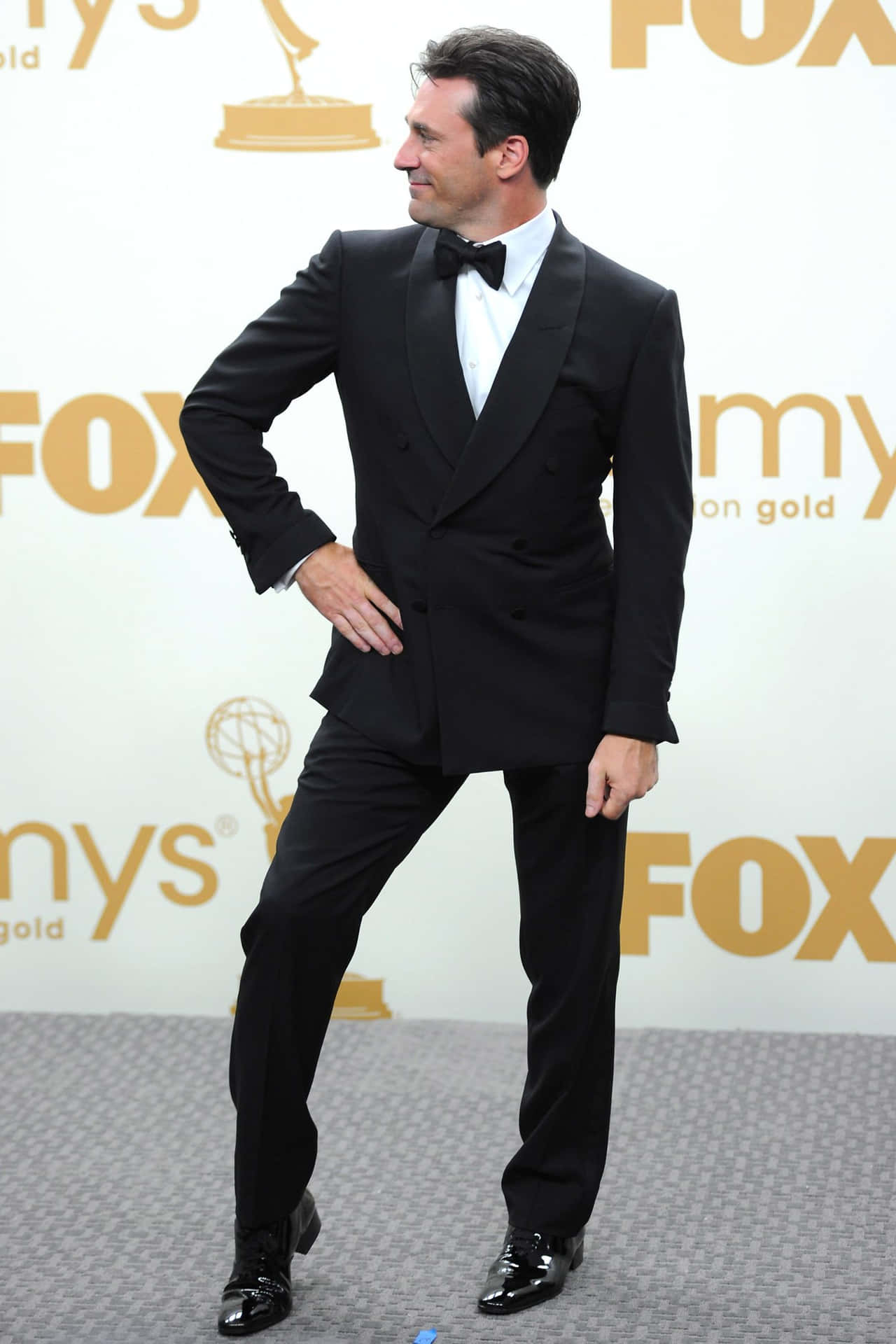 Jon Hamm 桌布 壁紙 — 一位身穿俐落黑色燕尾服配蝴蝶結的男士，在艾美獎紅地毯上自信擺姿勢，背景為FOX。