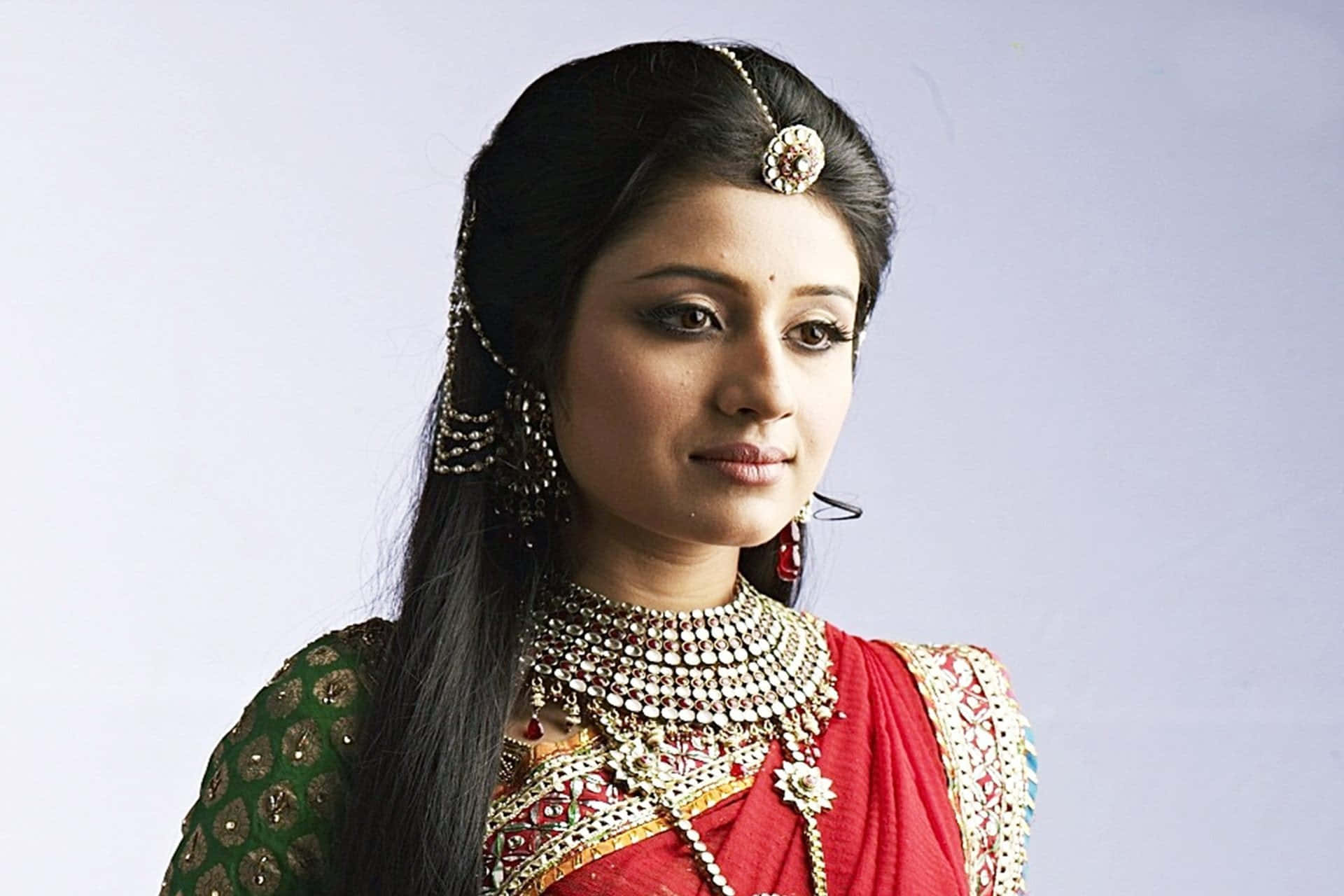 Indian Girl 桌布 壁紙 — 一位身穿傳統印度服飾、佩戴精緻珠寶、表情寧靜的女性，背景為純色。