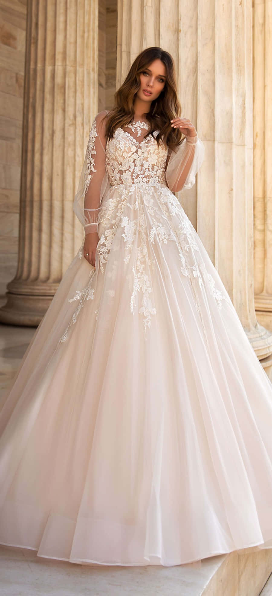 Wedding Dress 桌布 壁紙 — 一位身穿優雅象牙白蕾絲婚紗的女性，優雅地站在巨大的石柱之間。