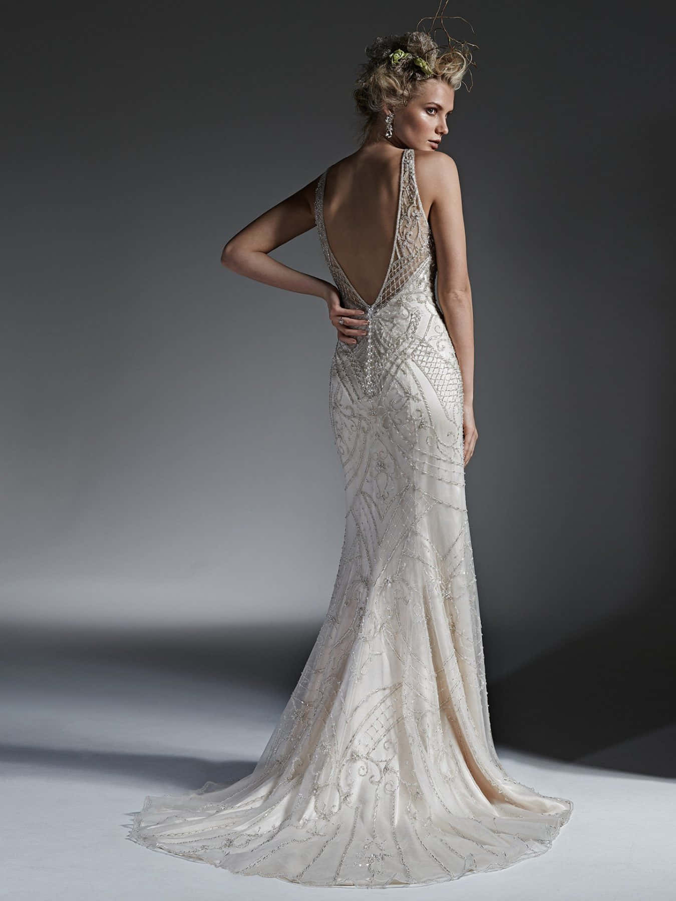 Wedding Dress 桌布 壁紙 — 一位身穿優雅象牙色珠飾長裙、背部深V剪裁的女性，在簡約灰色攝影棚背景下優雅擺姿勢。