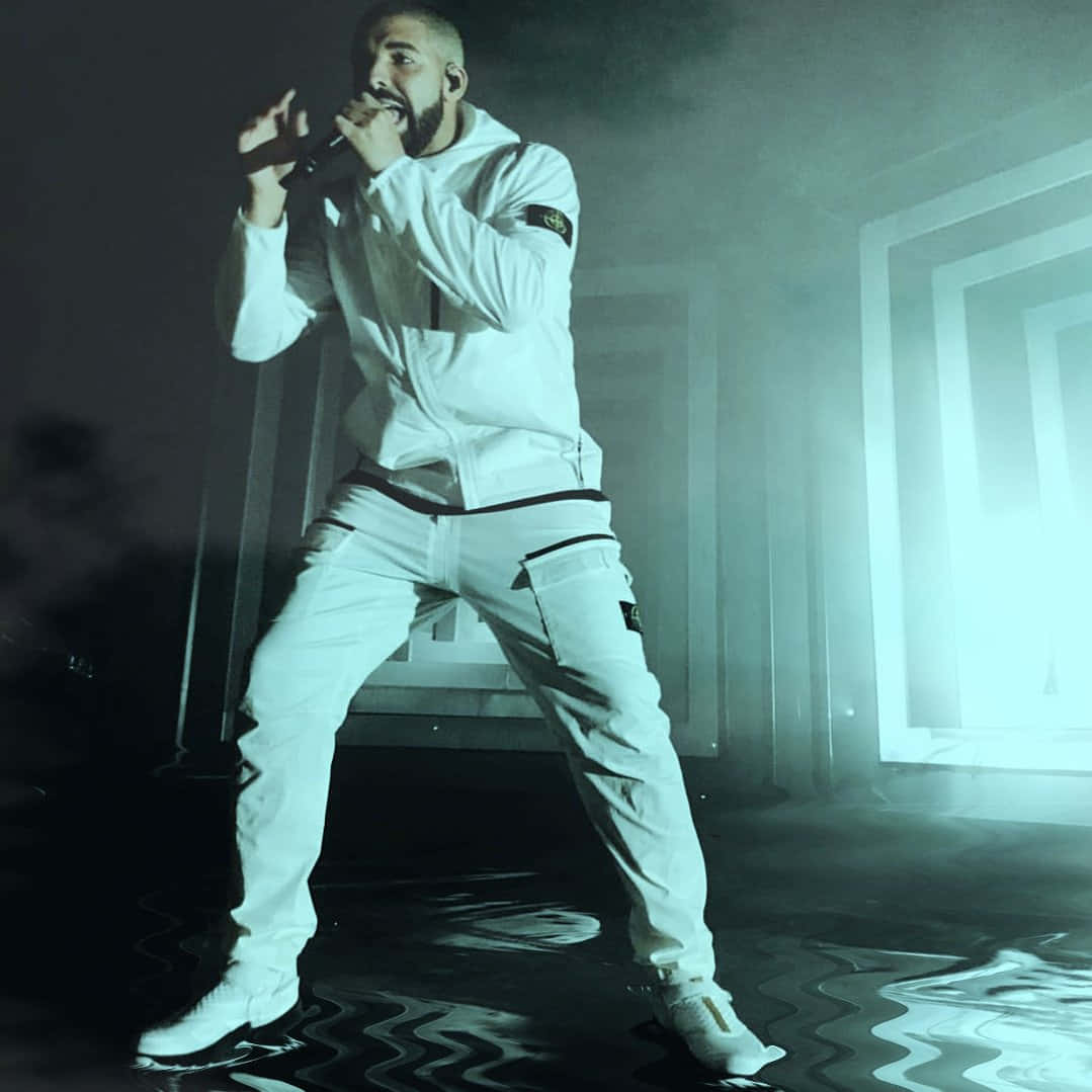 Drake 桌布 壁紙 — 一位身穿全白服裝的男表演者在充滿煙霧和反光地板的舞台上，在戲劇性燈光下對著麥克風唱歌。