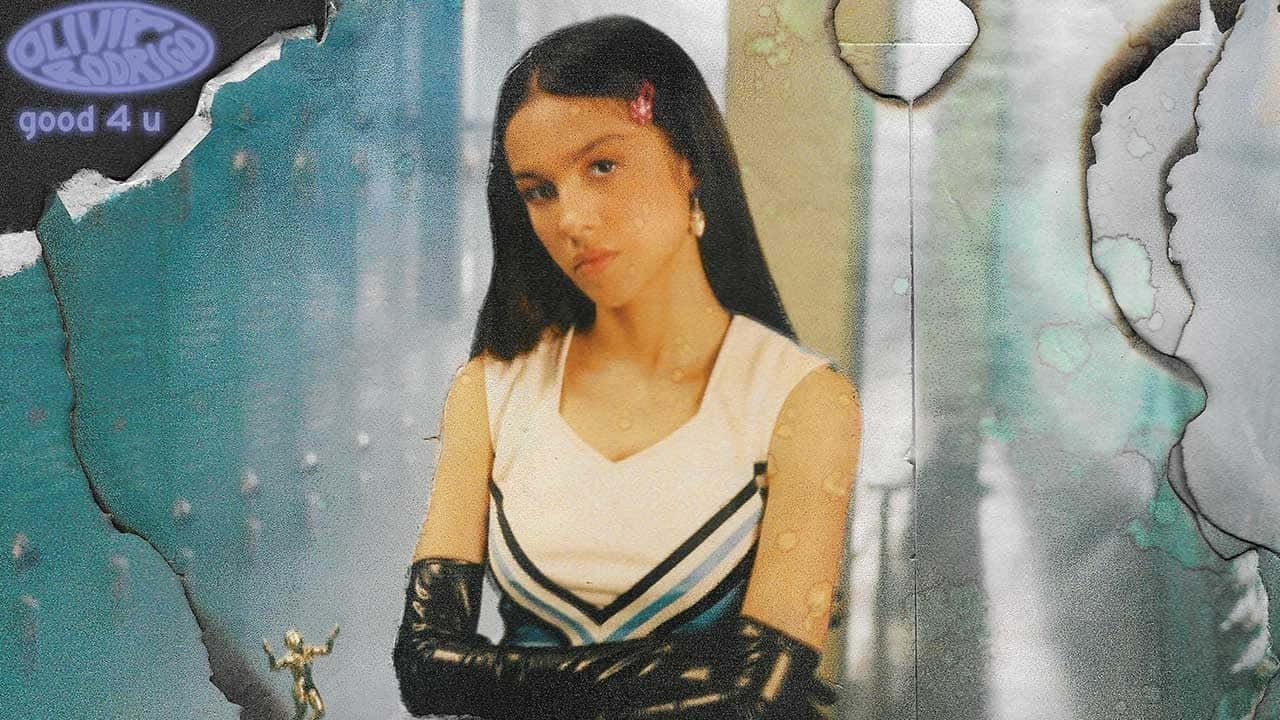 Olivia Rodrigo 桌布 壁紙 — 一位身穿啦啦隊服、戴黑色手套的年輕女性，在質感破損的青綠色和灰色背景前直視鏡頭。