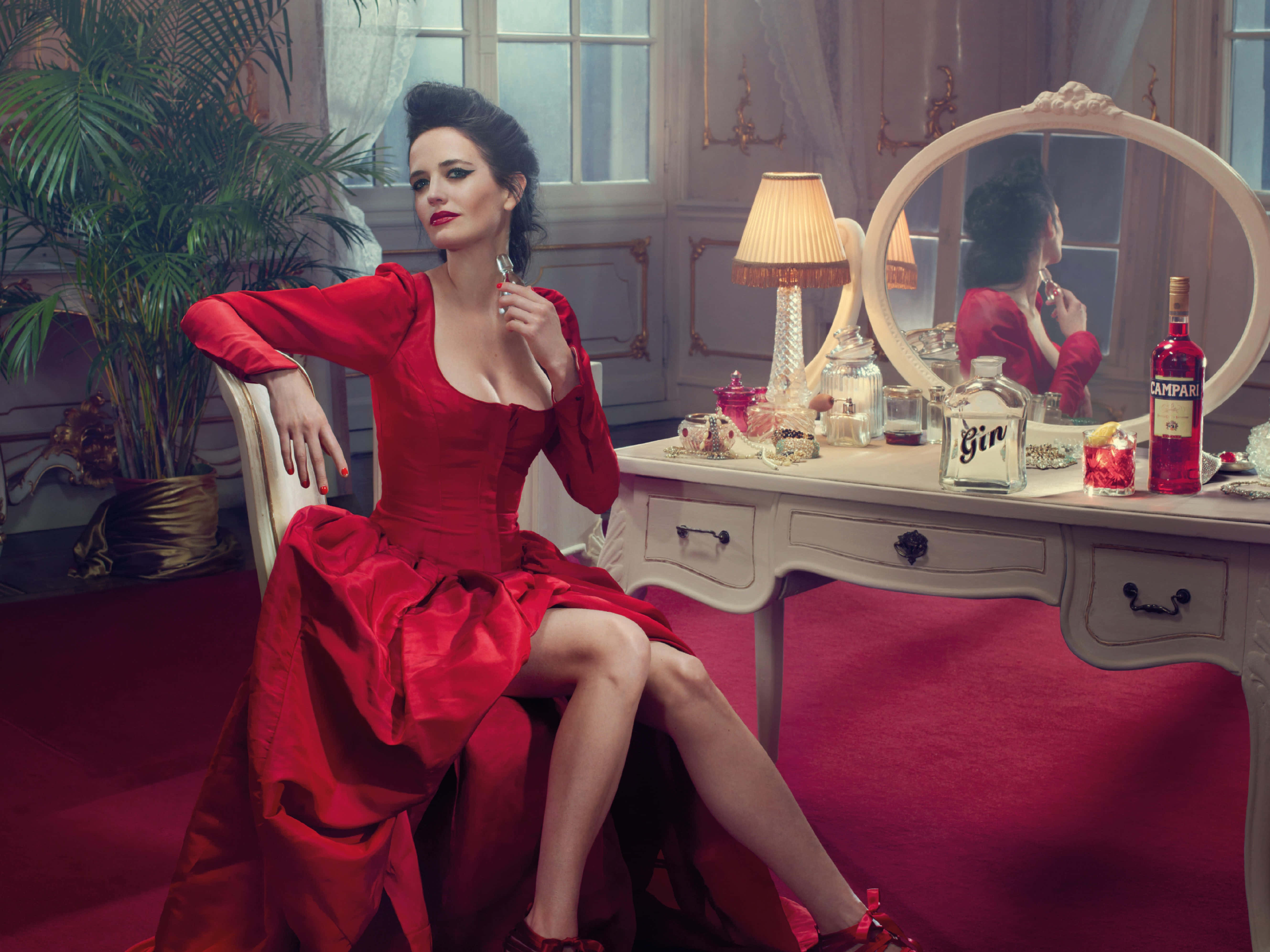 eva green 桌布 壁紙 — 一位身穿搶眼紅色緞面連衣裙的女性，優雅地坐在一張椅子上，身處一個配有梳妝鏡和琴酒的奢華復古房間。