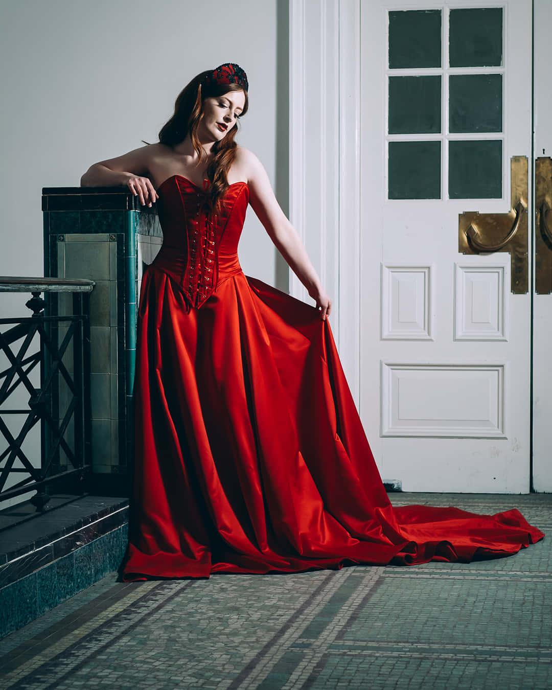 Red Wedding 桌布 壁紙 — 一位身穿搶眼紅色緞面長裙的女性，在經典室內設計中優雅地靠在一扇復古門旁。