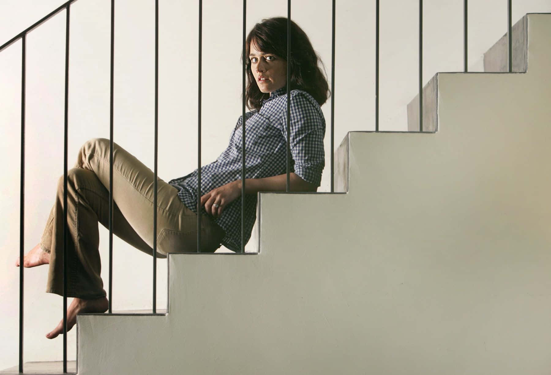 Robin Tunney 桌布 壁紙 — 一位身穿格仔恤衫嘅女人赤腳坐喺由黑色金屬欄杆框住嘅簡約混凝土樓梯上。