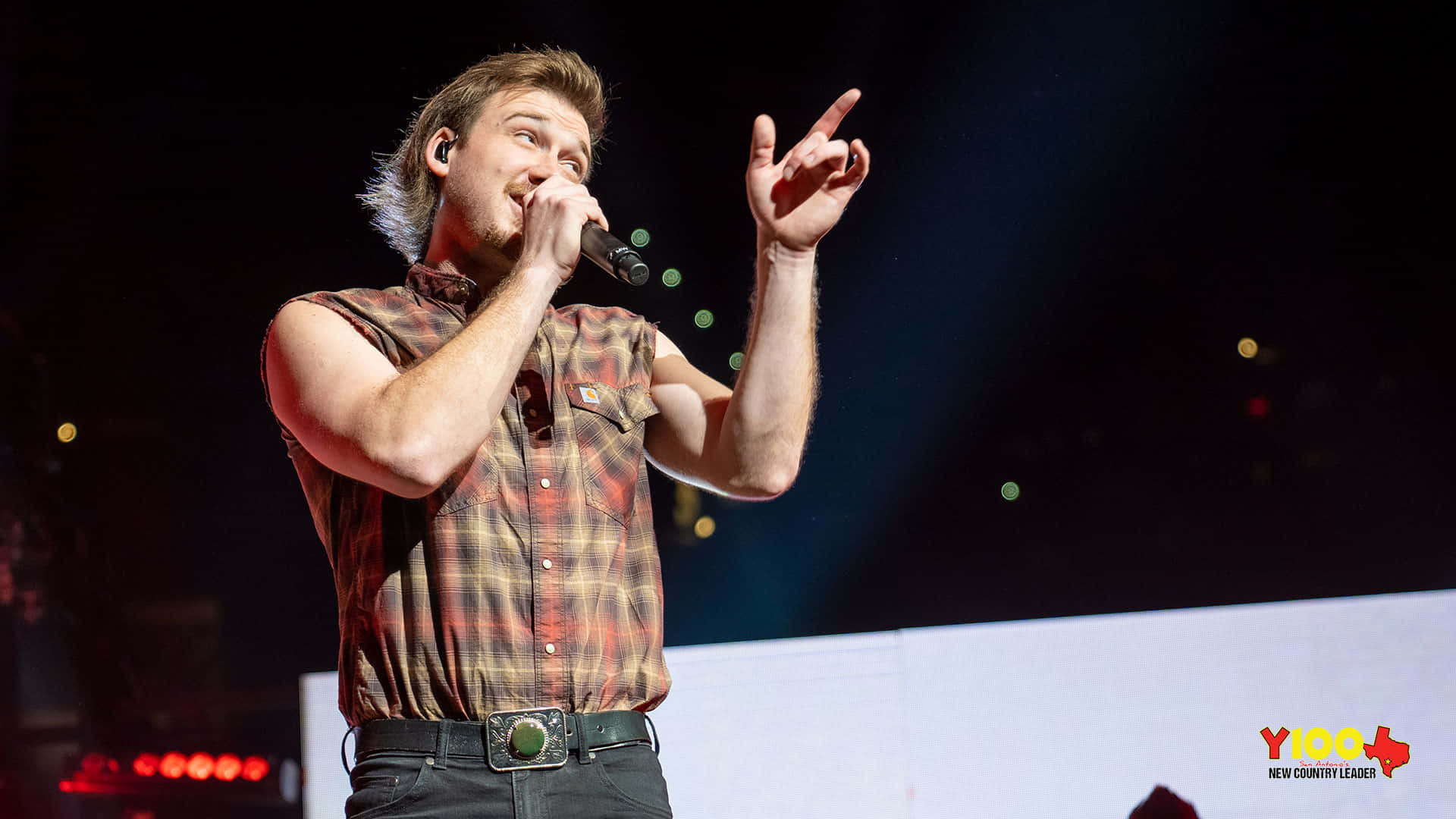 Morgan Wallen 桌布 壁紙 — 一位身穿格仔恤衫的男鄉村歌手在明亮的舞台燈光下熱情地表演。