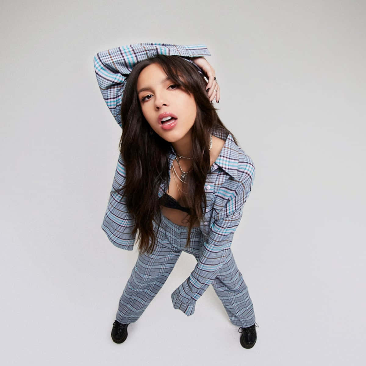 Olivia Rodrigo 桌布 壁紙 — 一位身穿格紋西裝的年輕女性在純白背景上頑皮地將襯衫平衡在頭上。