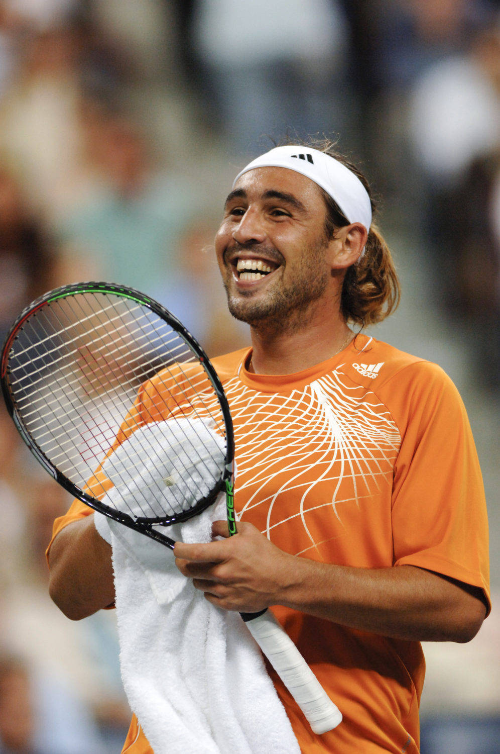 Marcos Baghdatis Expressing Joy on Court 壁紙 — 一位身穿橙色襯衫的快樂網球運動員在比賽中拿著球拍和毛巾大笑。